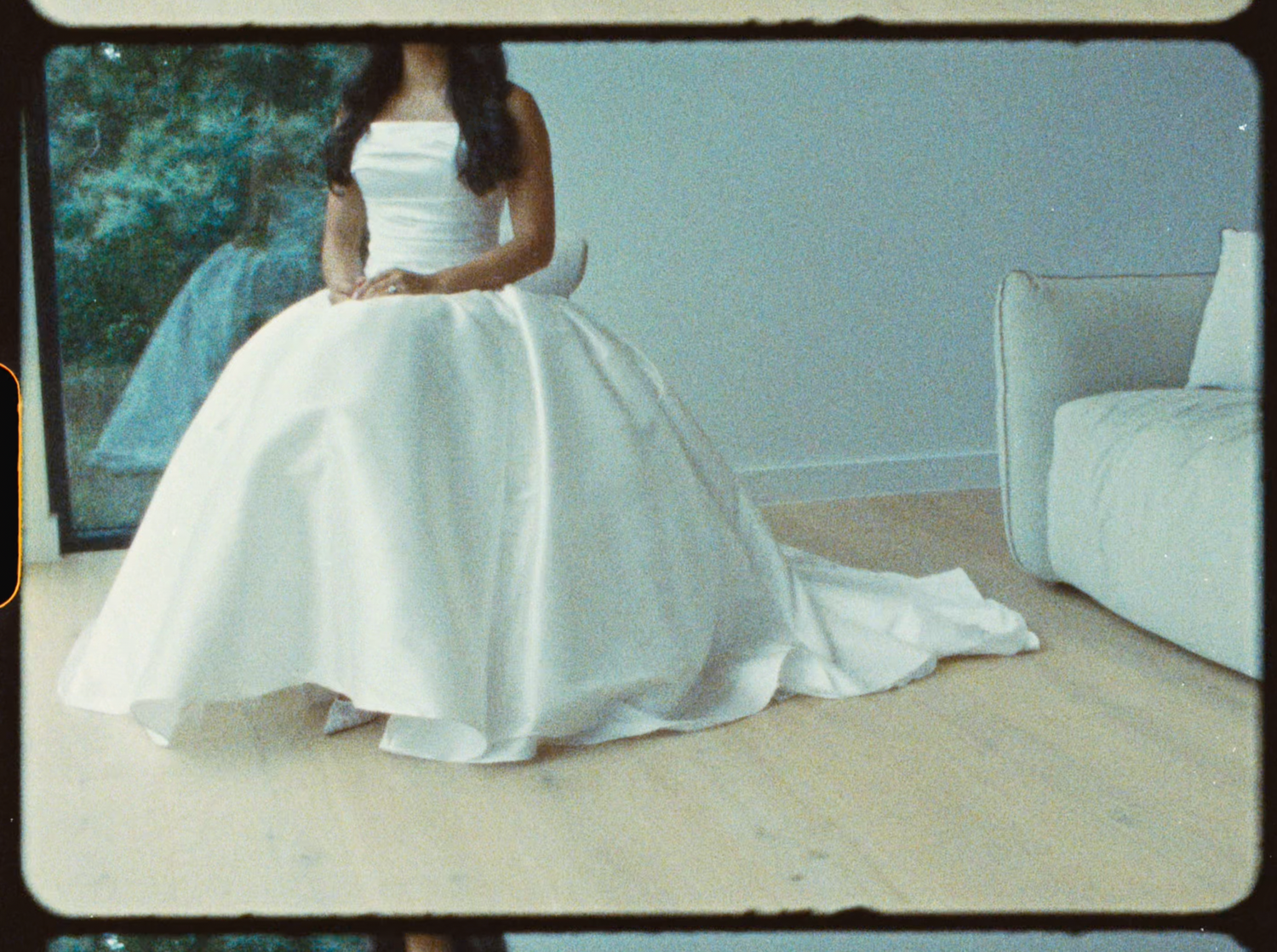 Bride in a strapless white ball gown with a full skirt and train, sitting elegantly on a wooden floor.