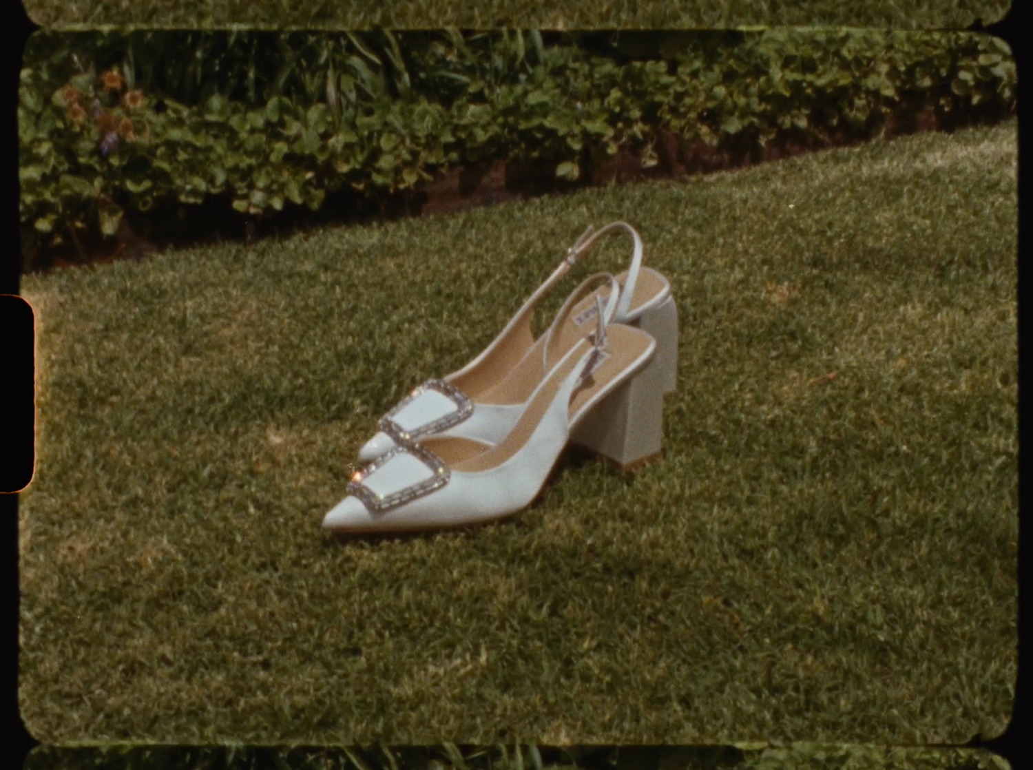 White crystal-embellished slingback bridal heels placed on green grass outdoors.