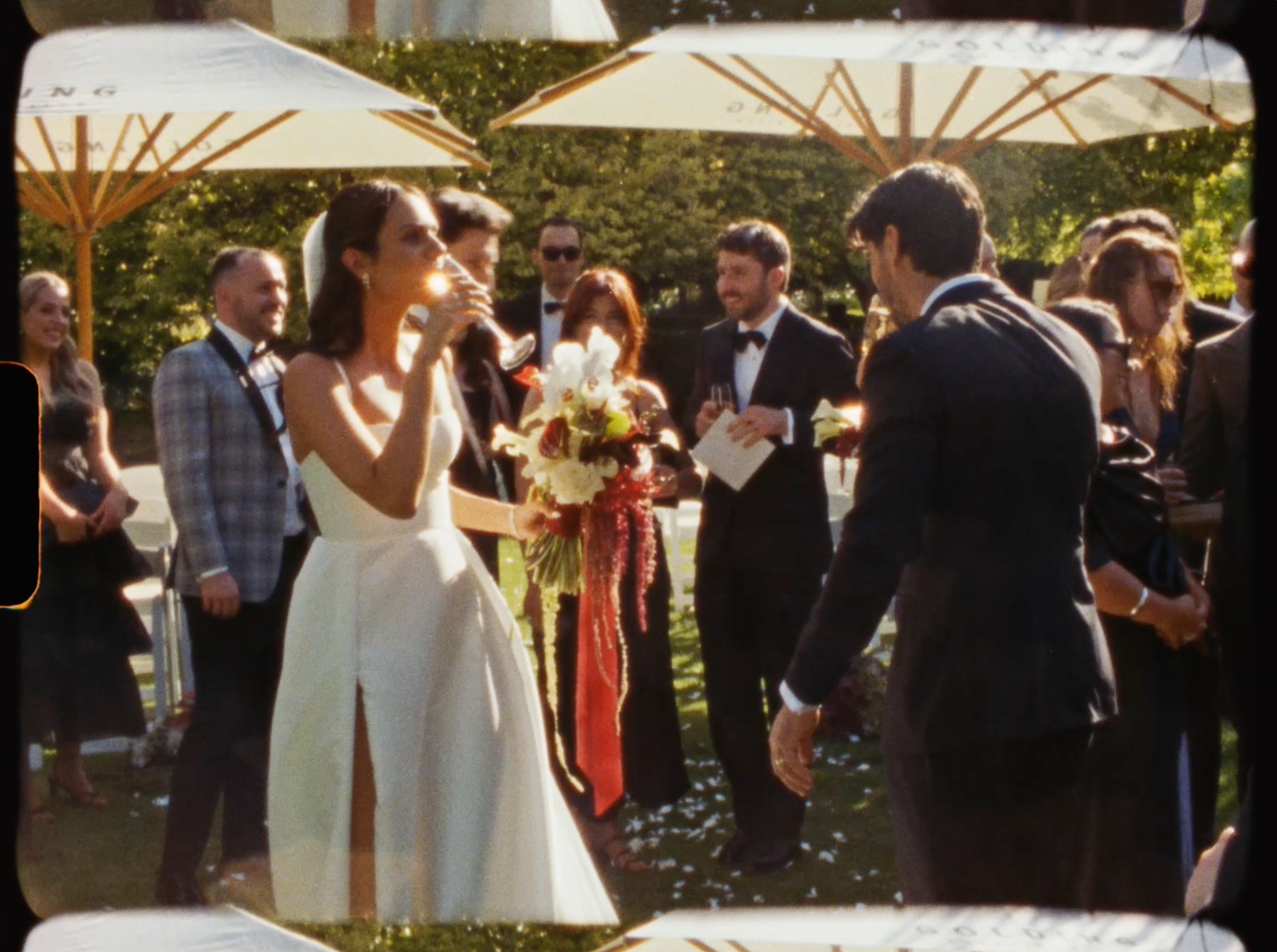 Bride and groom exchanging vows outdoors surrounded by wedding guests in a sunlit garden ceremony.