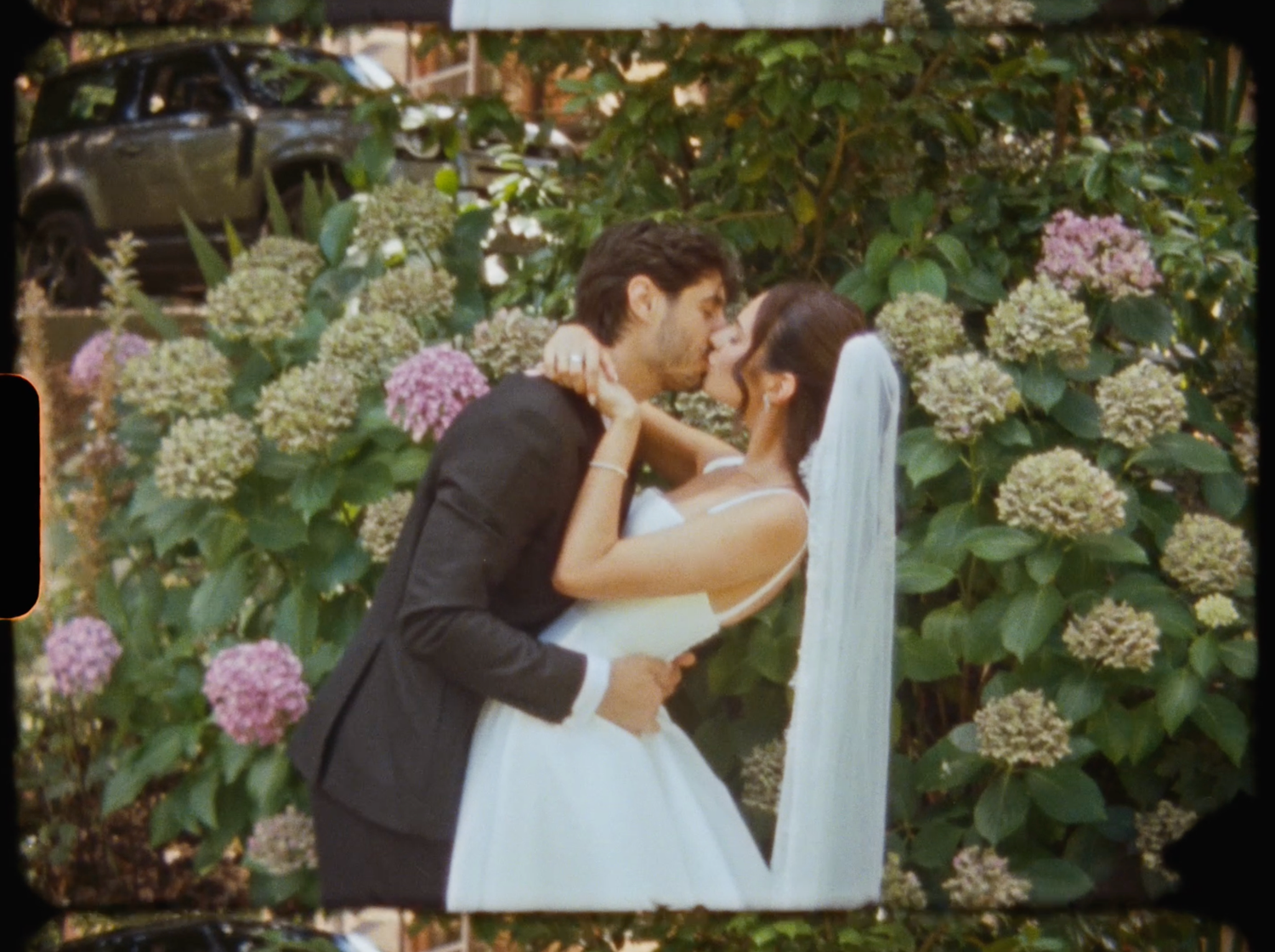 Bride and groom sharing a romantic kiss surrounded by blooming hydrangeas in a garden.