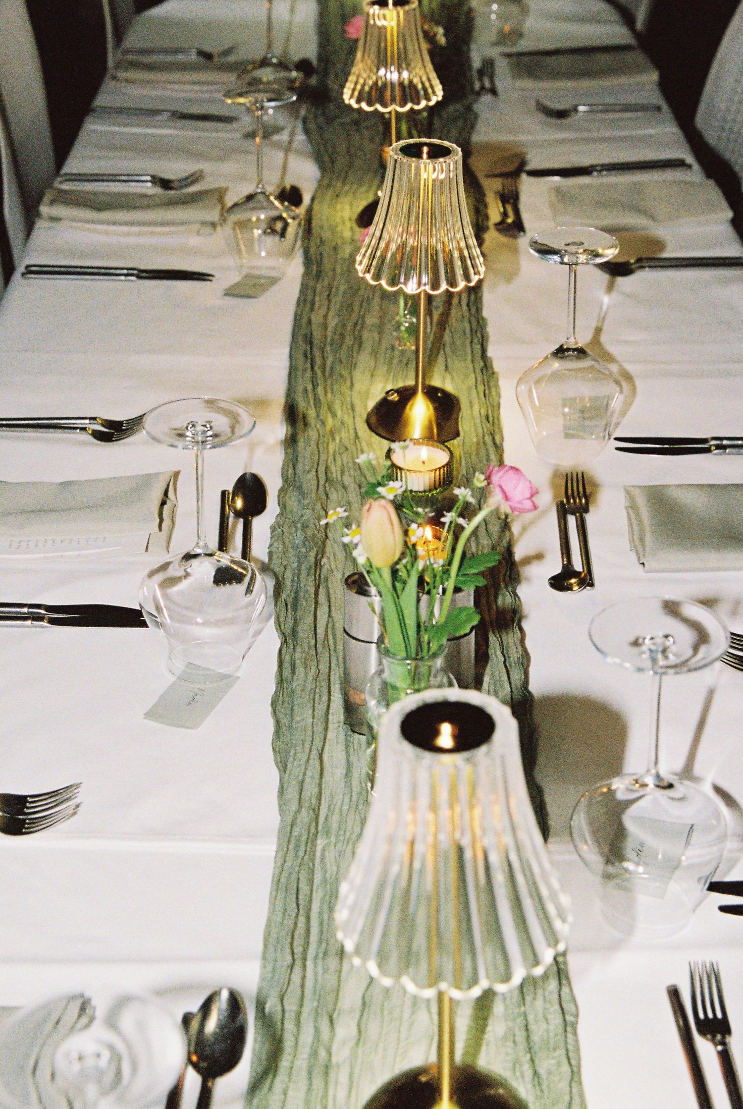 Elegant wedding reception table with green runner, gold lamp centerpieces, and crystal glassware.