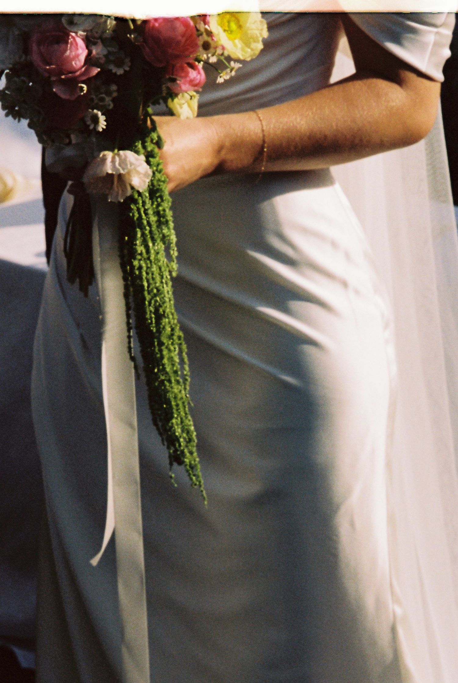 Bride in elegant white gown holds a colorful bridal bouquet with cascading greenery and ribbon.