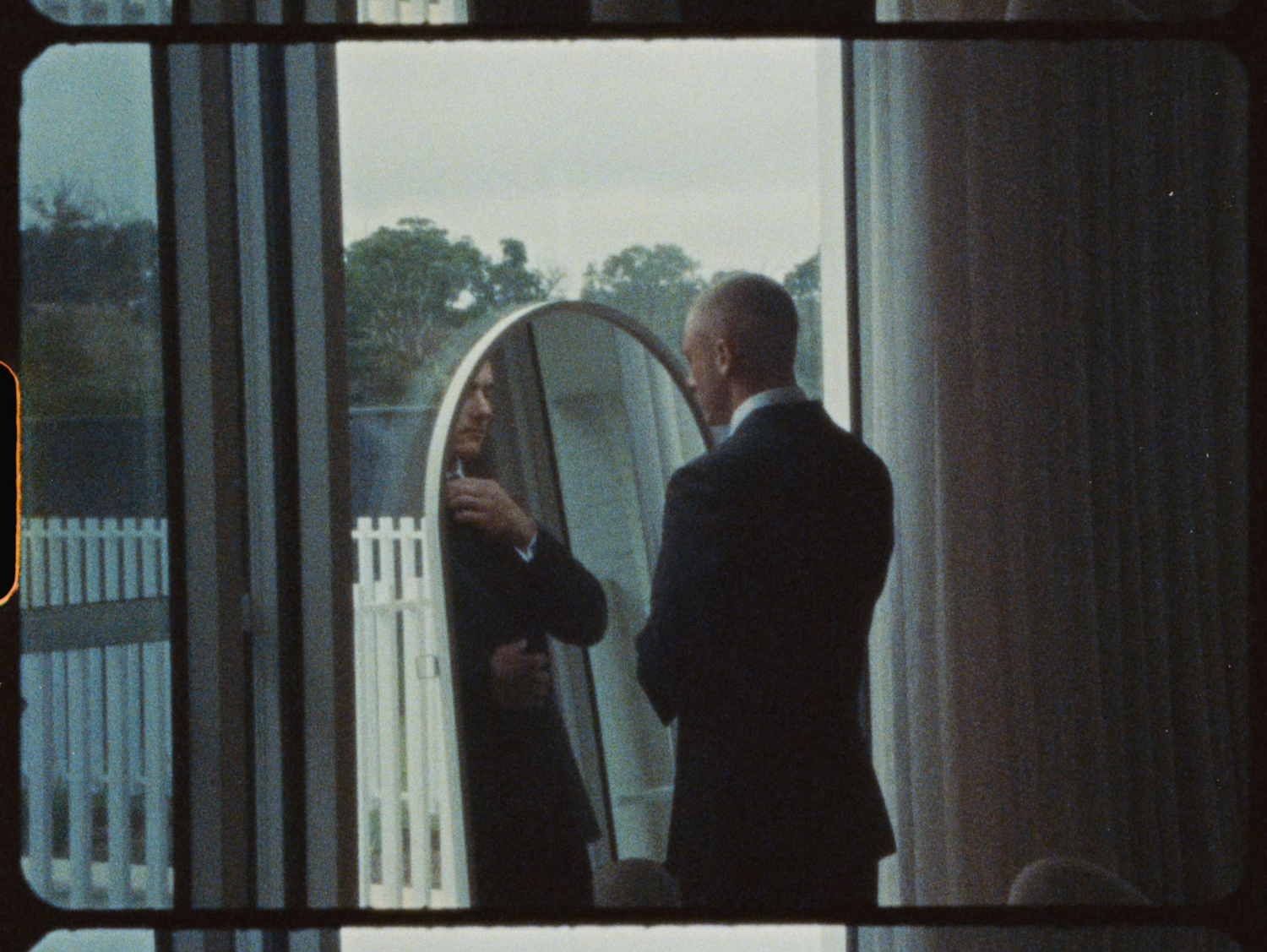 Man in dark suit checking his appearance in an oval mirror before wedding ceremony.