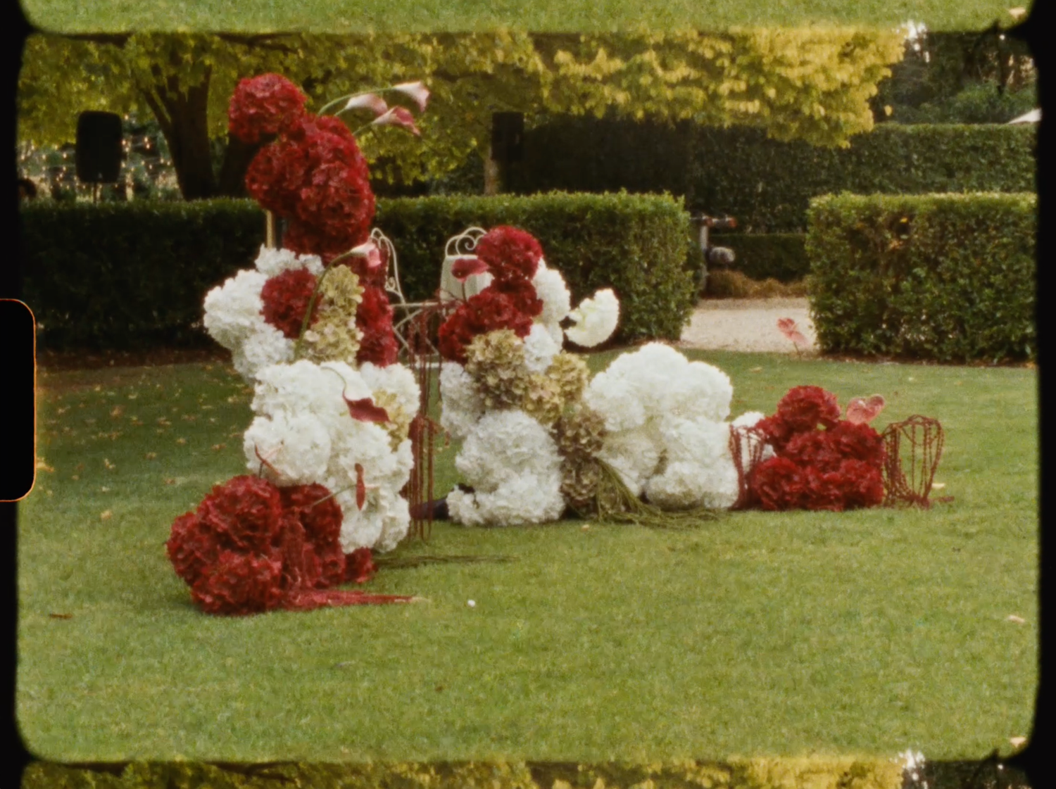 Vintage film-style photo of red, white, and gold floral wedding decorations arranged on a lawn.