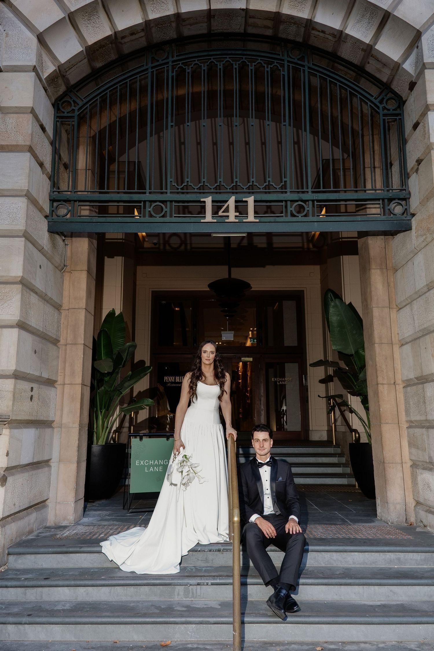 Bride and groom posing on steps outside building 141, Exchange Lane, bride in white gown, groom in black tuxedo.
