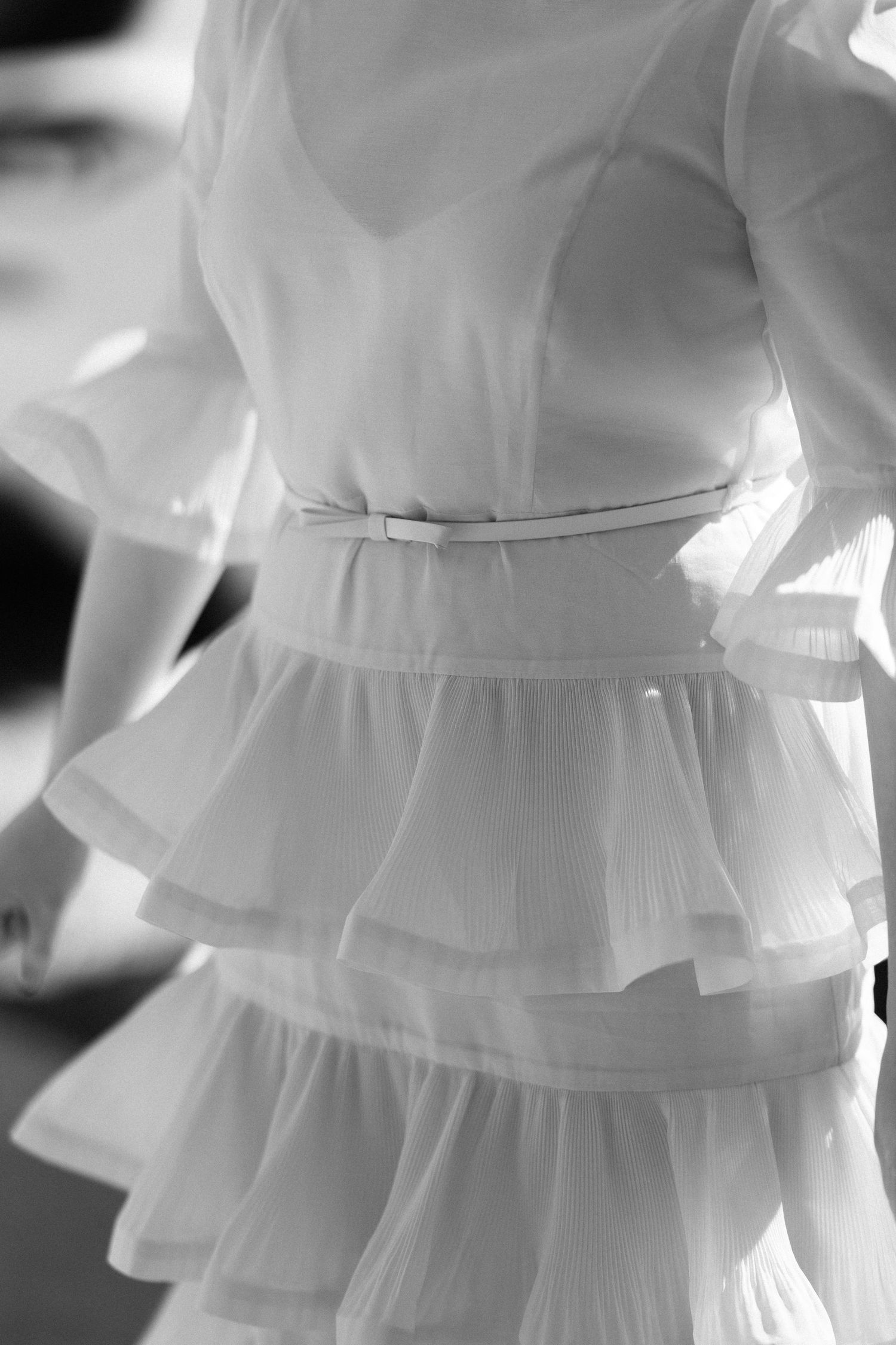 Close-up black and white detail of brides tiered ruffled wedding dress with delicate belt.