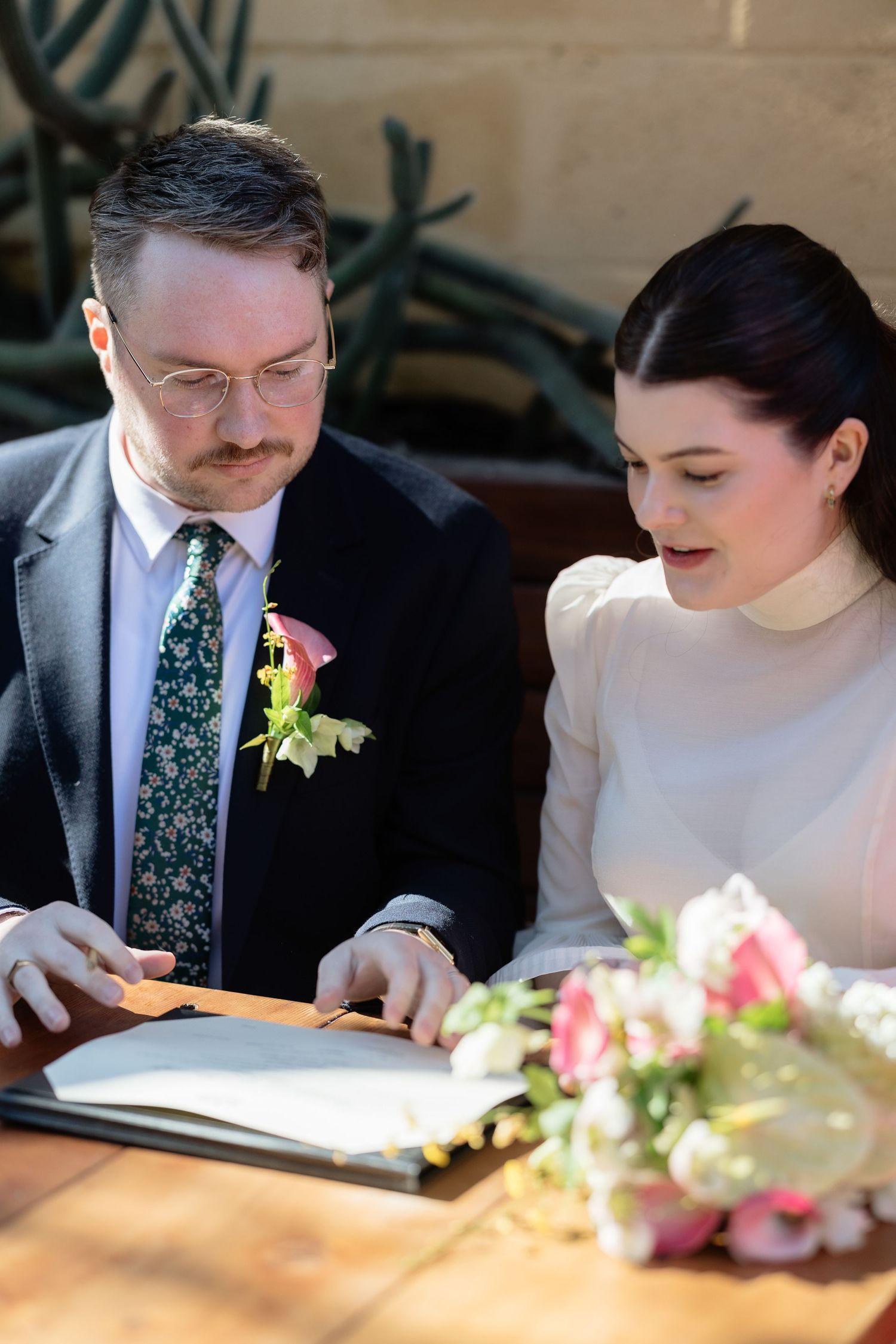 Bride and groom signing wedding register together, with floral bouquet in foreground.