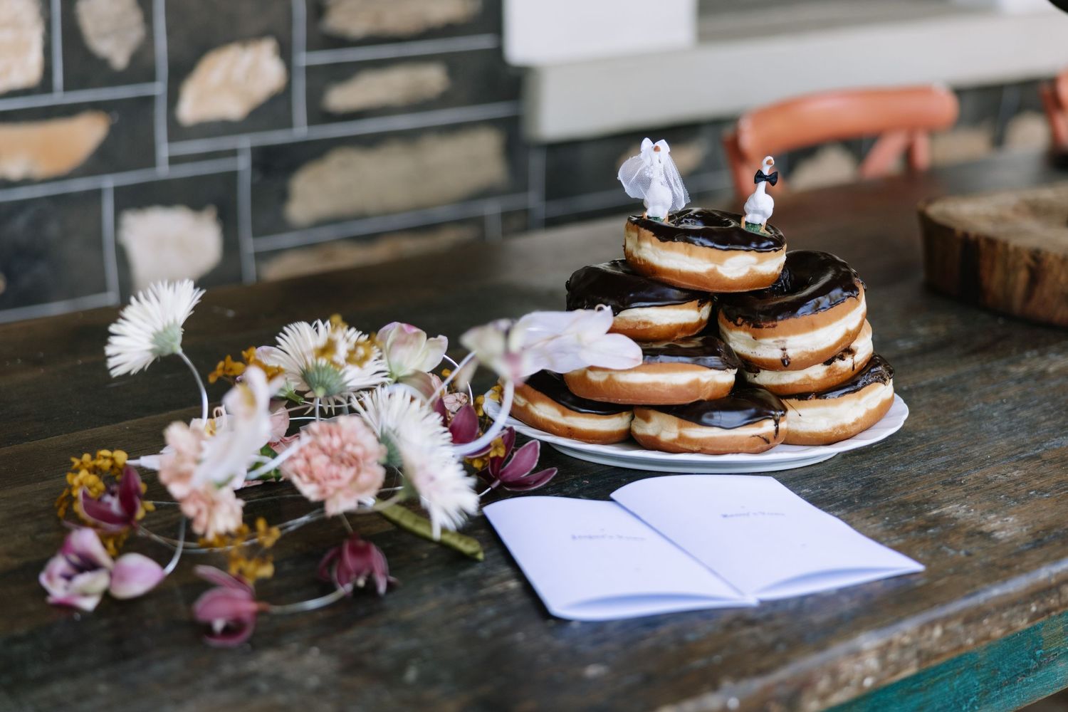 Wedding donut cake with bride and groom topper on rustic table with open guestbook and floral arrangement.