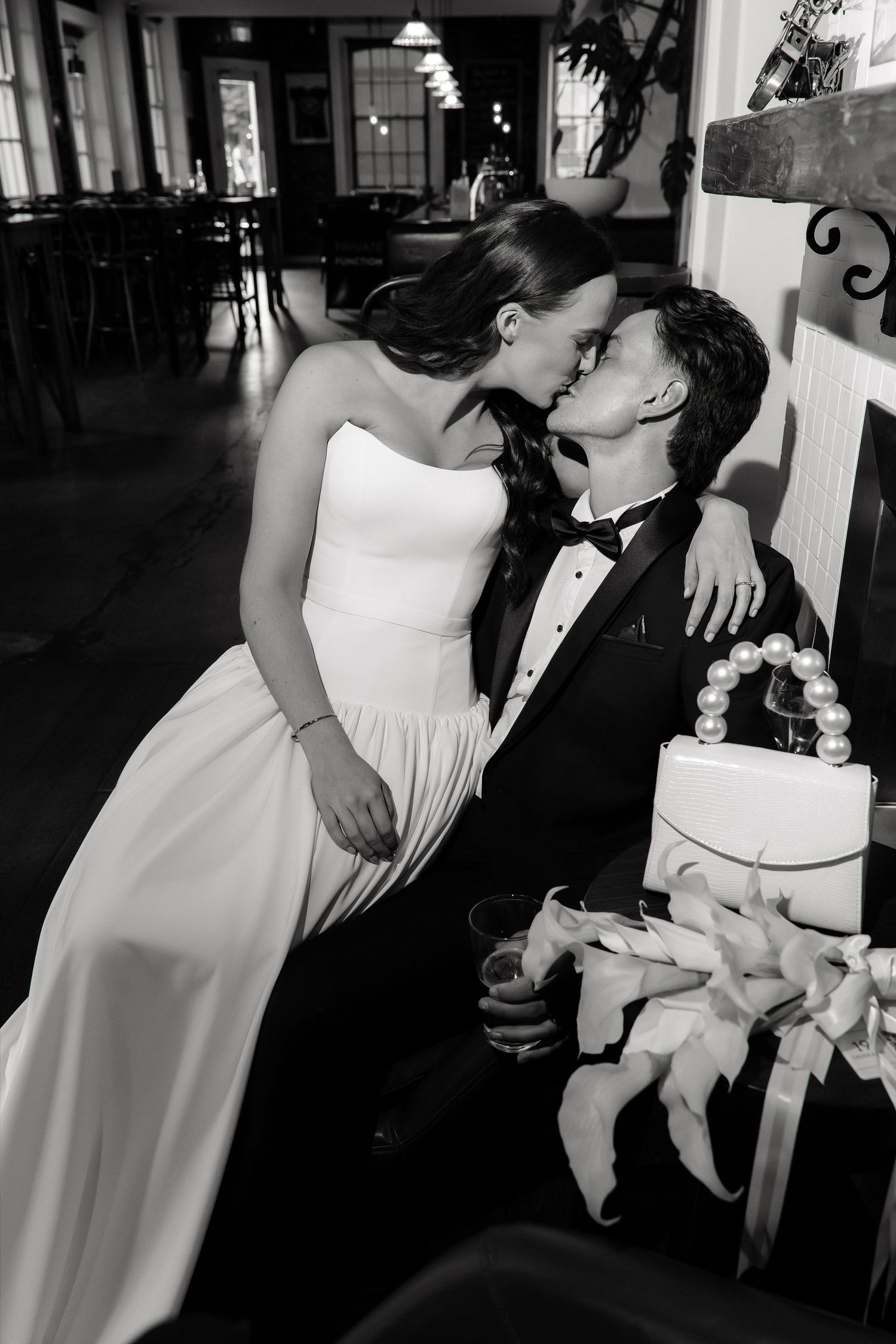 Black and white photo of a bride and groom sharing a kiss beside their wedding cake.