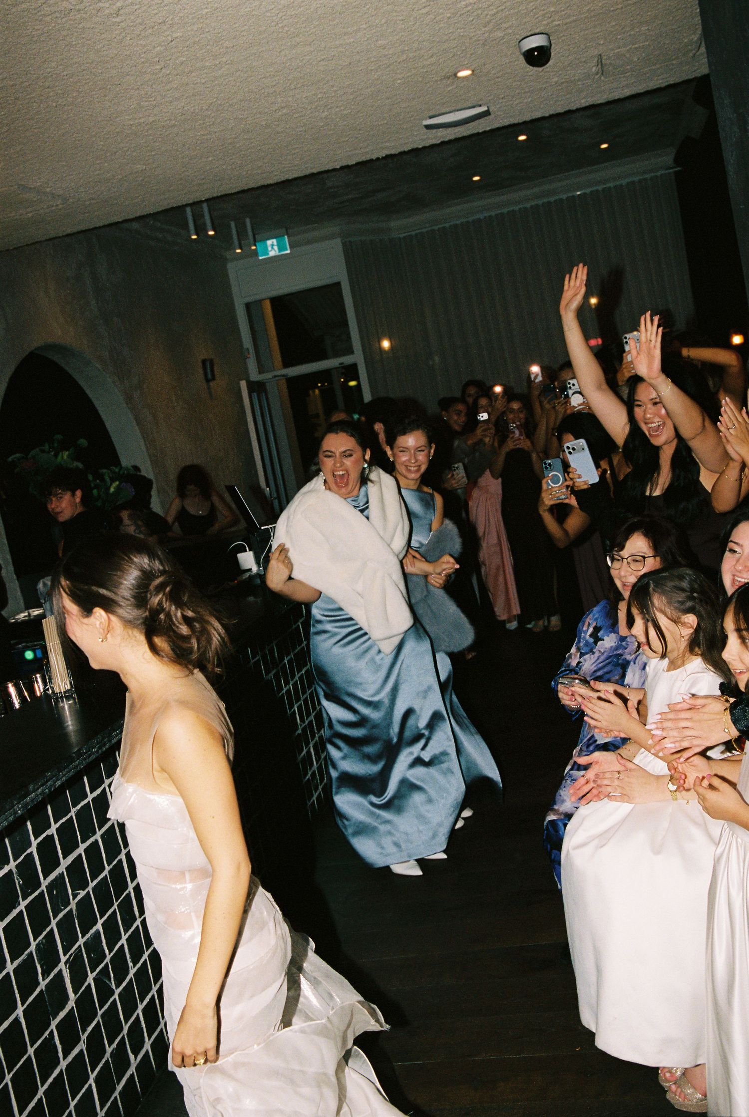 Guests celebrating at wedding reception with bride in white gown and dancing crowd.