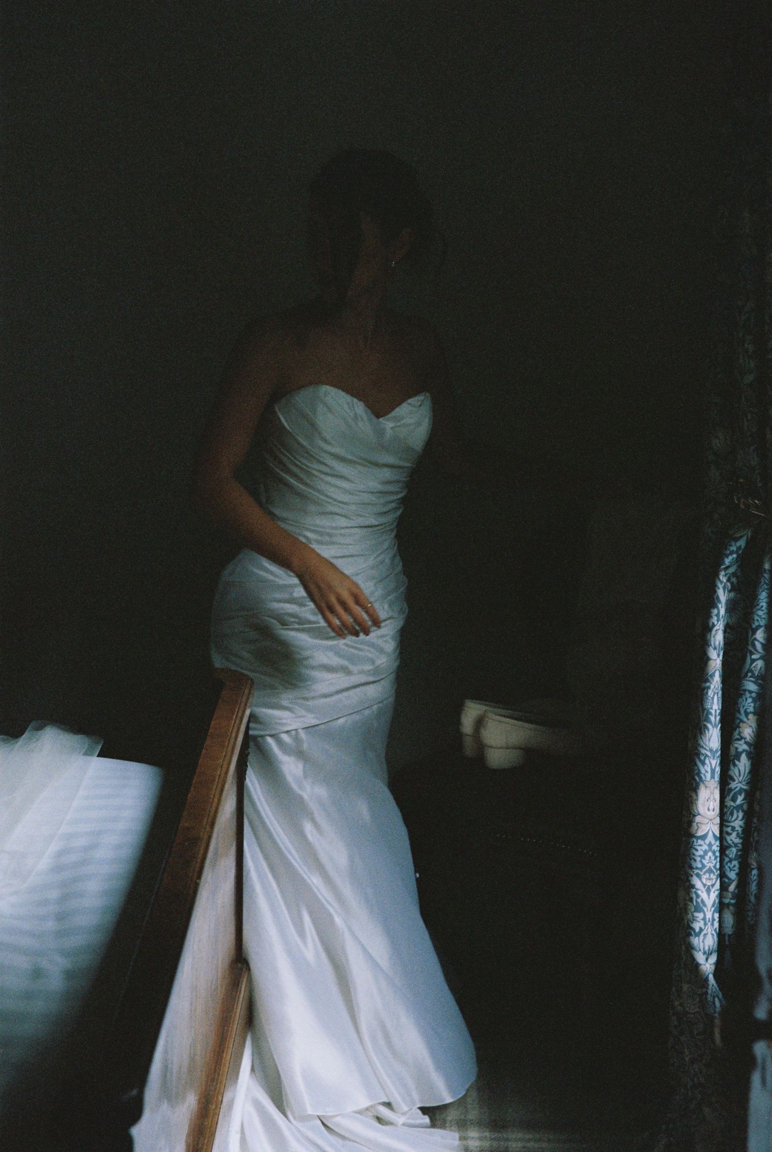 Bride in strapless white mermaid wedding gown standing in dramatic dark stairwell lighting.