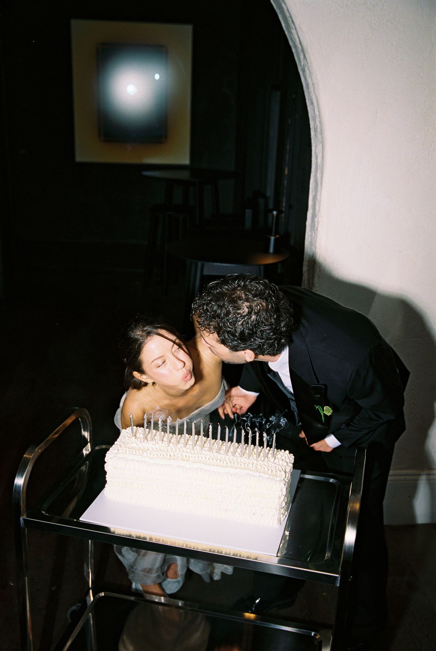 Couple sharing a kiss over a white wedding cake with candles at their elegant reception.