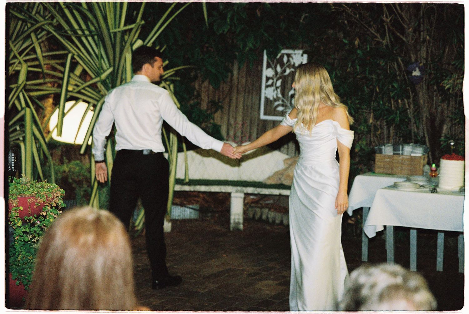 Newlywed couple holding hands during their first dance at an outdoor garden wedding reception.