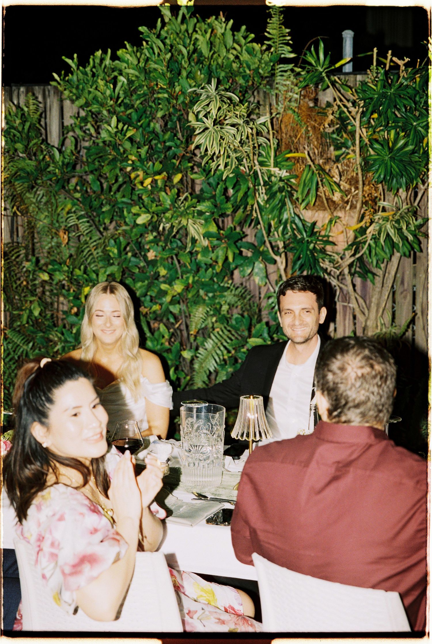 Wedding guests enjoying outdoor evening dinner reception surrounded by lush tropical greenery.