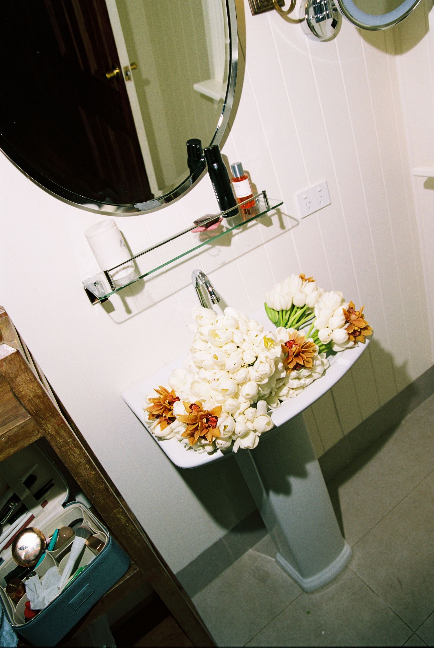 White tulips and orange flowers arranged in a pedestal bathroom sink as wedding decor.