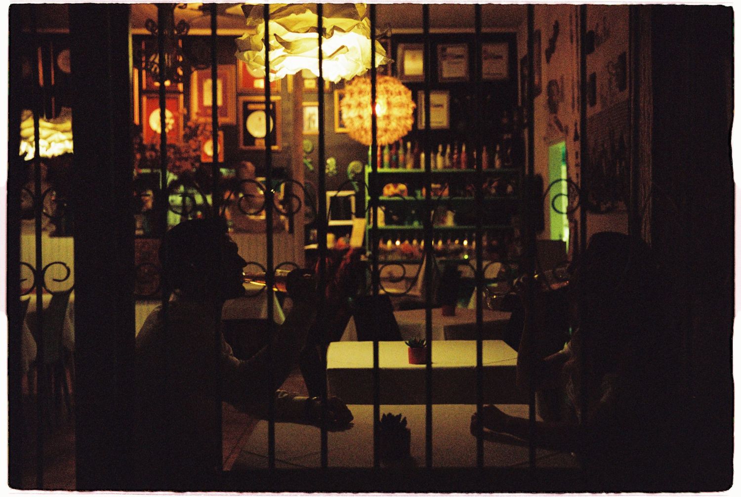 Silhouettes of people gathered outside a warmly lit bar or restaurant at night.