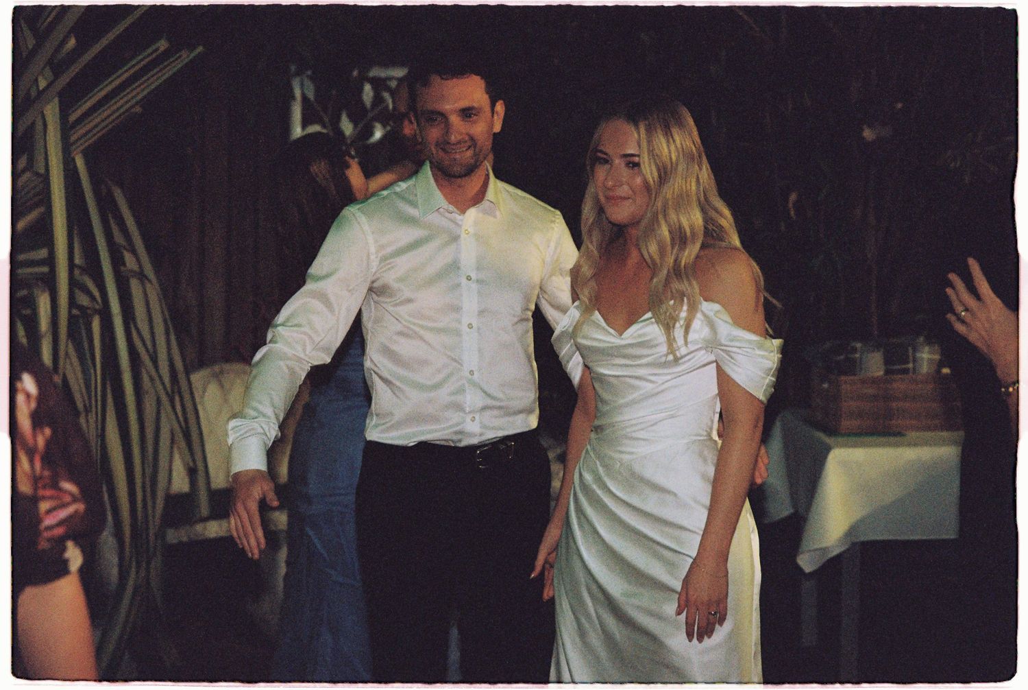Bride in white off-shoulder gown and groom in white shirt make grand entrance at elegant wedding reception.