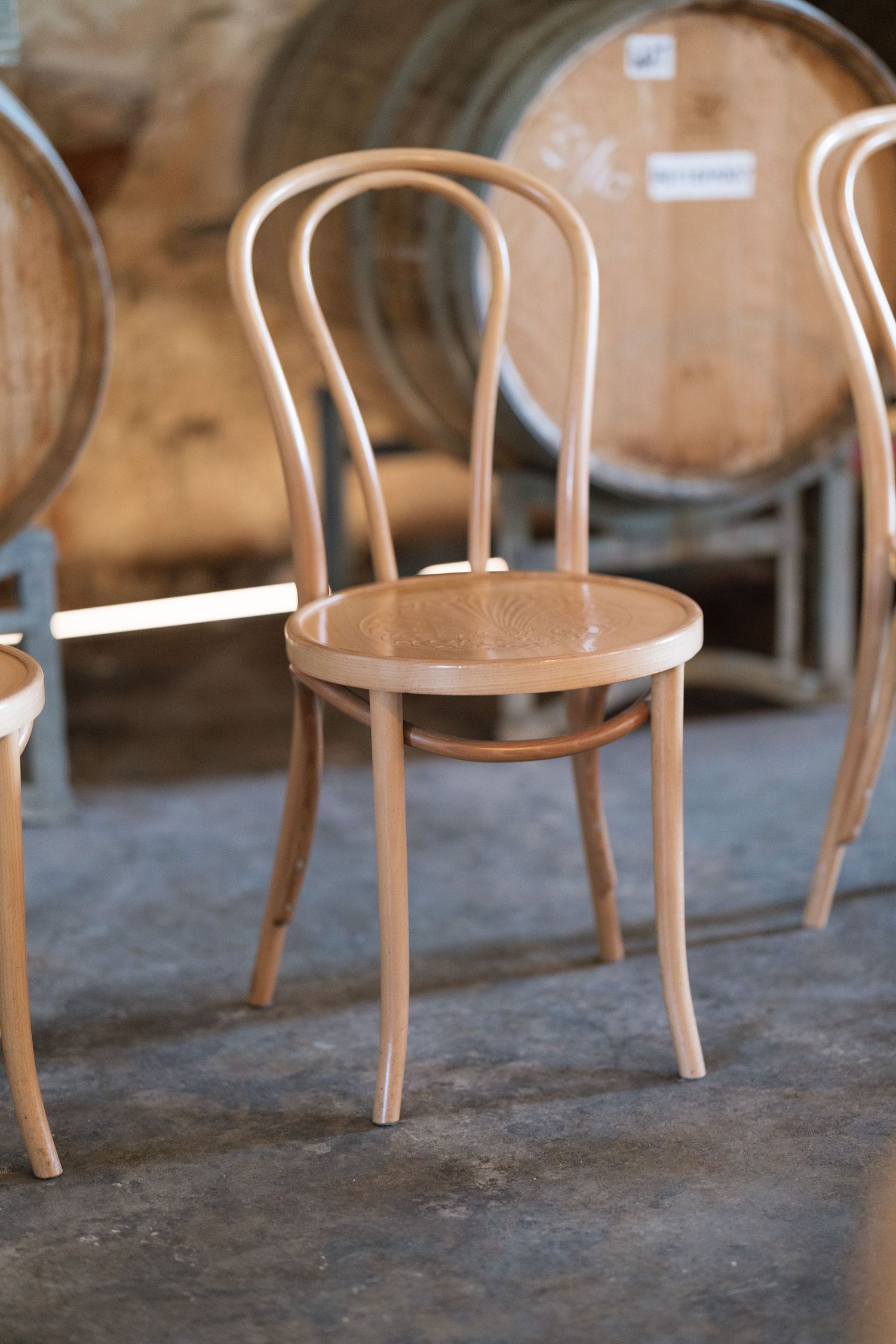 Elegant bentwood cafe chairs arranged in a rustic winery ceremony space with oak barrels in the background.