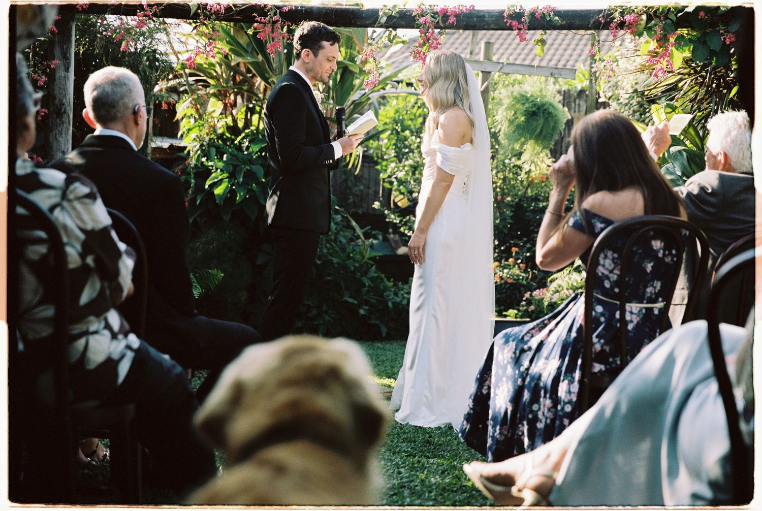 Outdoor garden wedding ceremony with couple exchanging vows among lush tropical greenery.