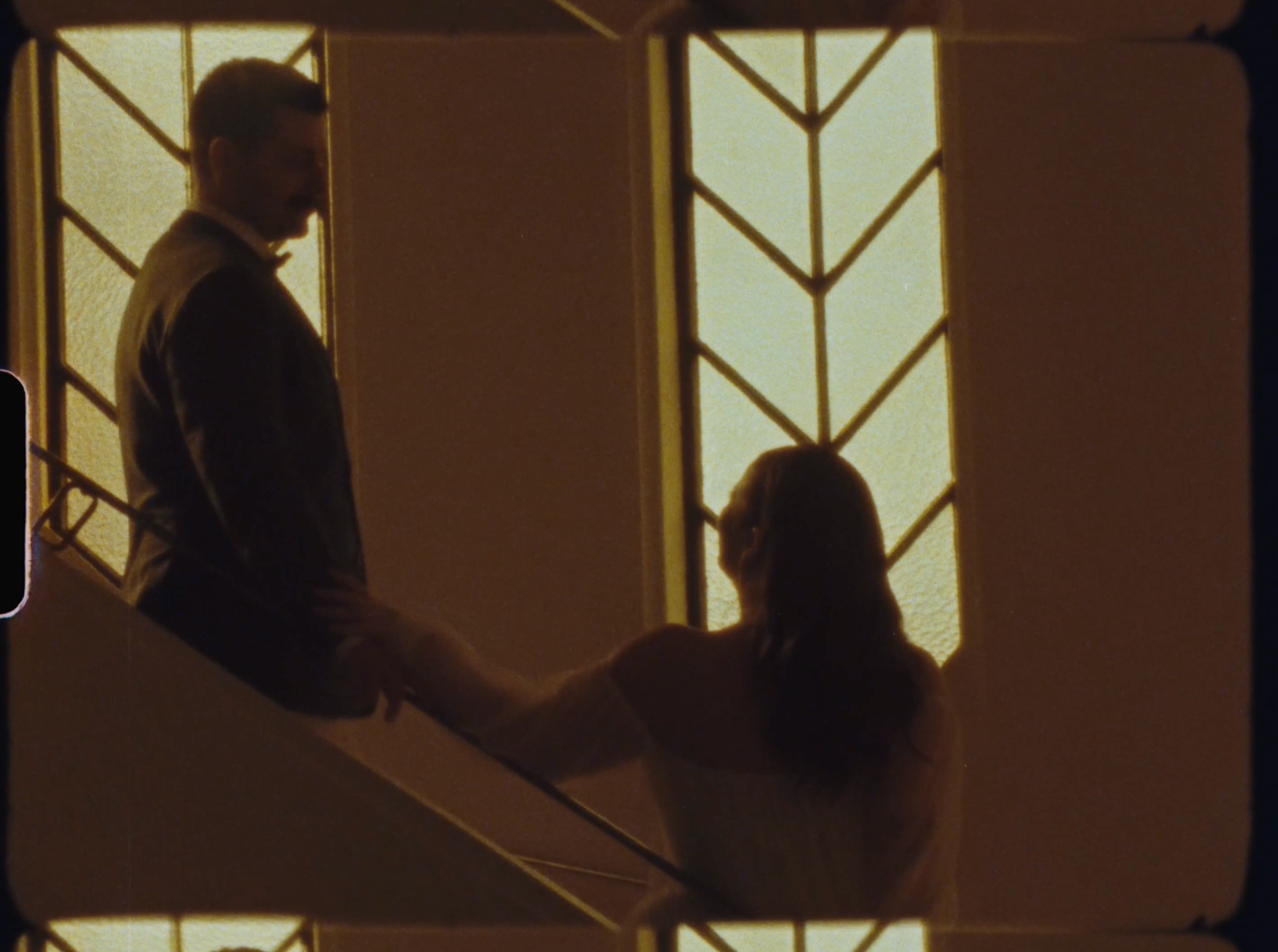 Romantic silhouette of a couple on stairs bathed in golden art deco stained glass window light.