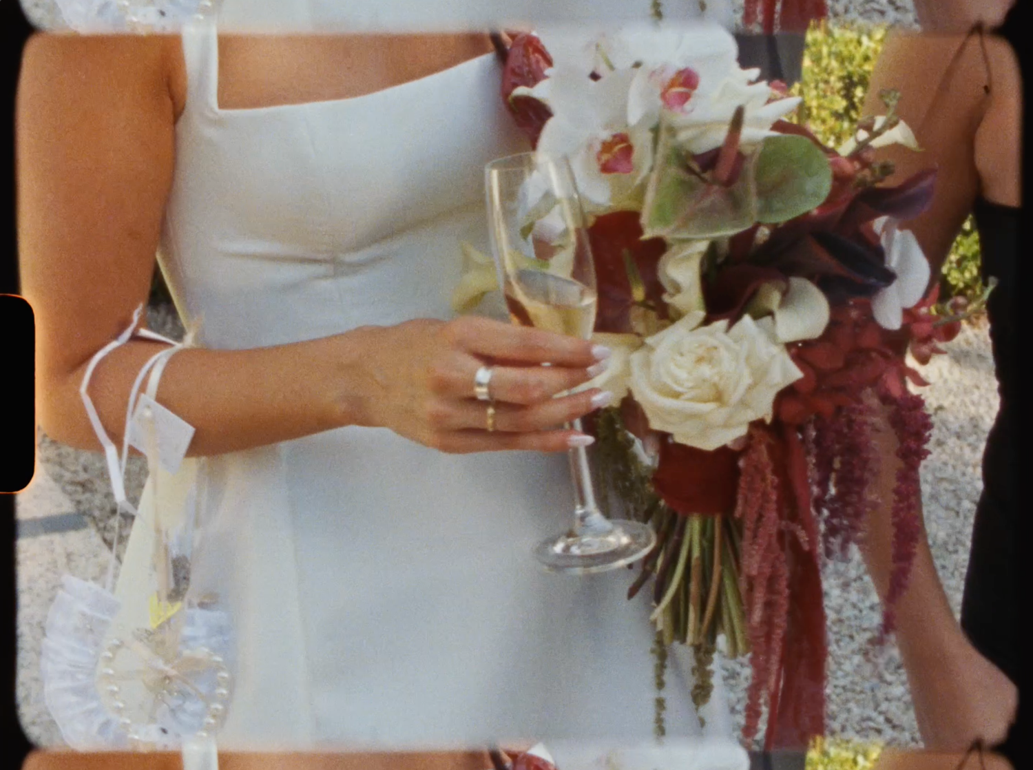 Bride in white dress holding champagne flute and elegant bouquet of white and burgundy flowers at wedding.