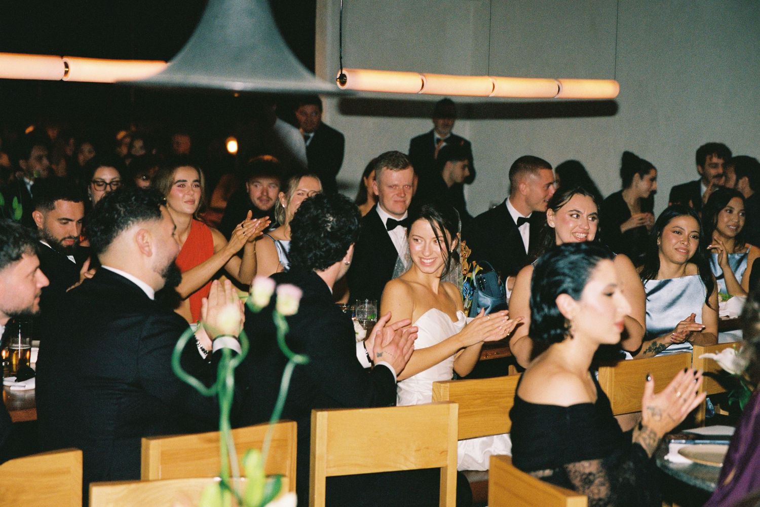 Wedding guests applauding and celebrating at an elegant indoor reception dinner.