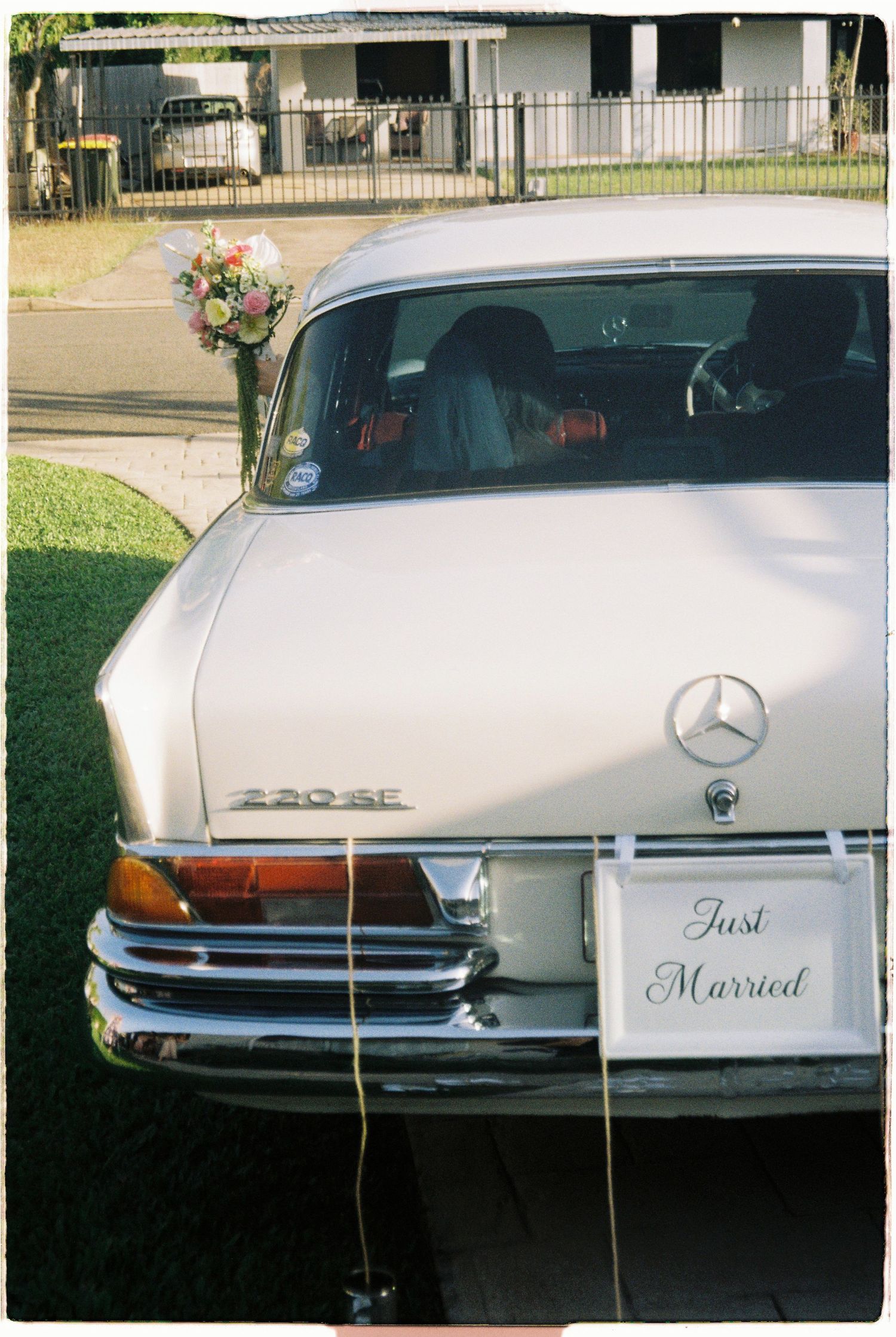 Vintage white Mercedes-Benz decorated with Just Married sign and floral bouquet on trunk.