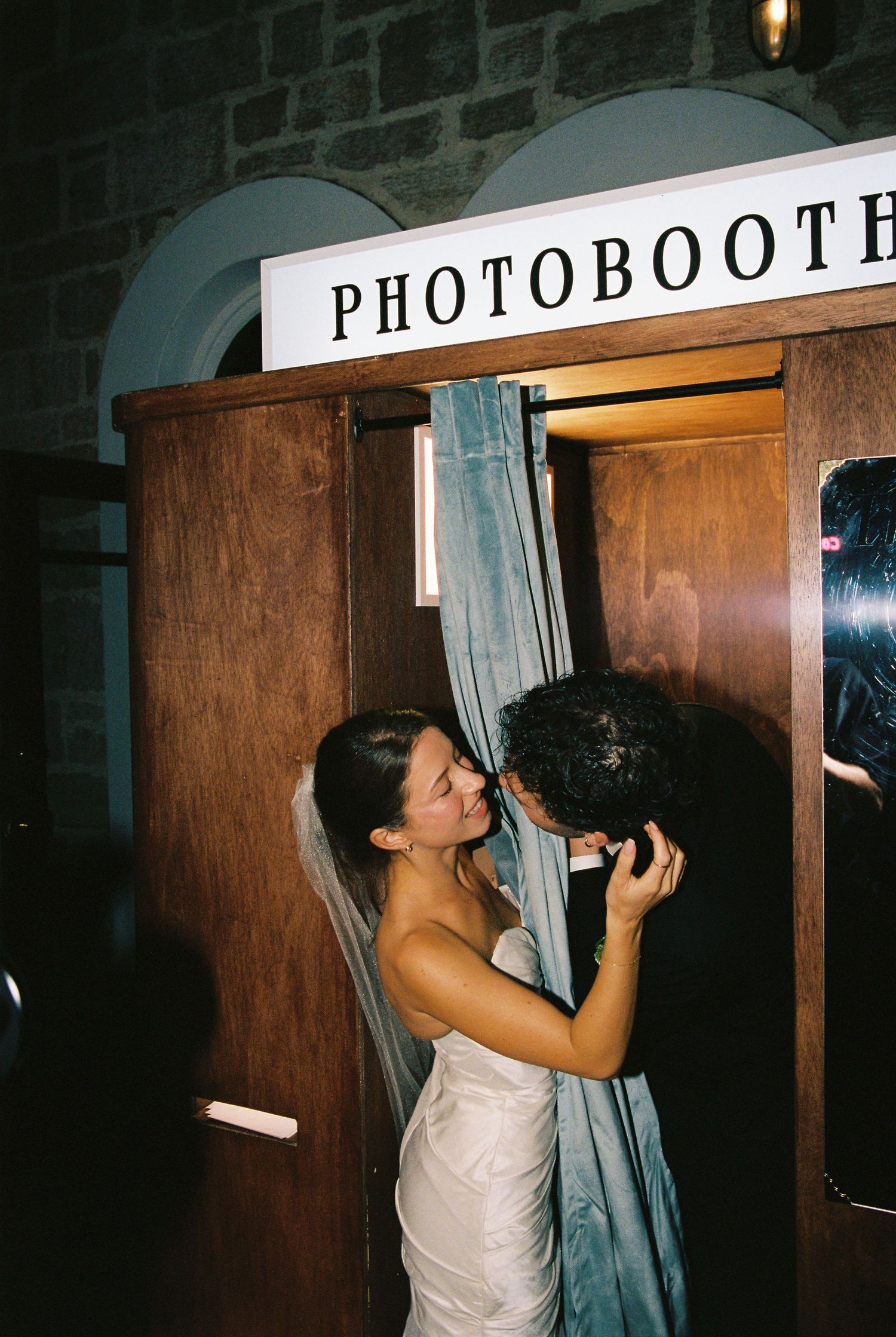 Bride and groom sharing a kiss at a wooden photobooth during their wedding reception.