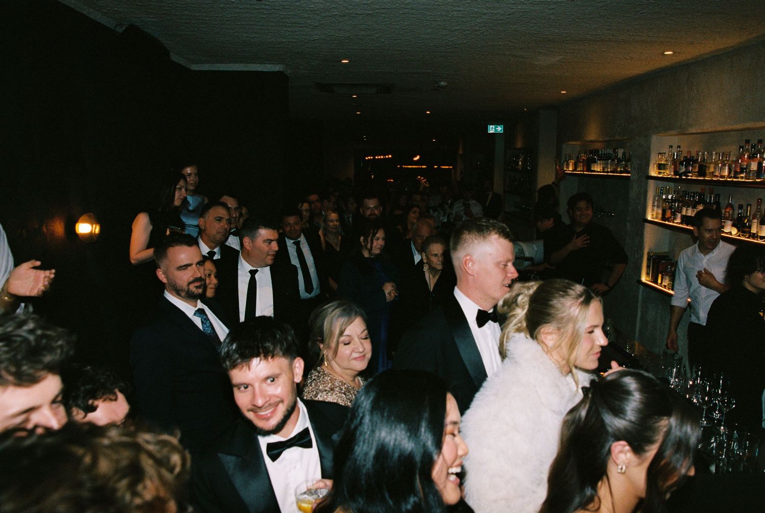 Formally dressed wedding guests mingle and celebrate near a well-stocked bar.