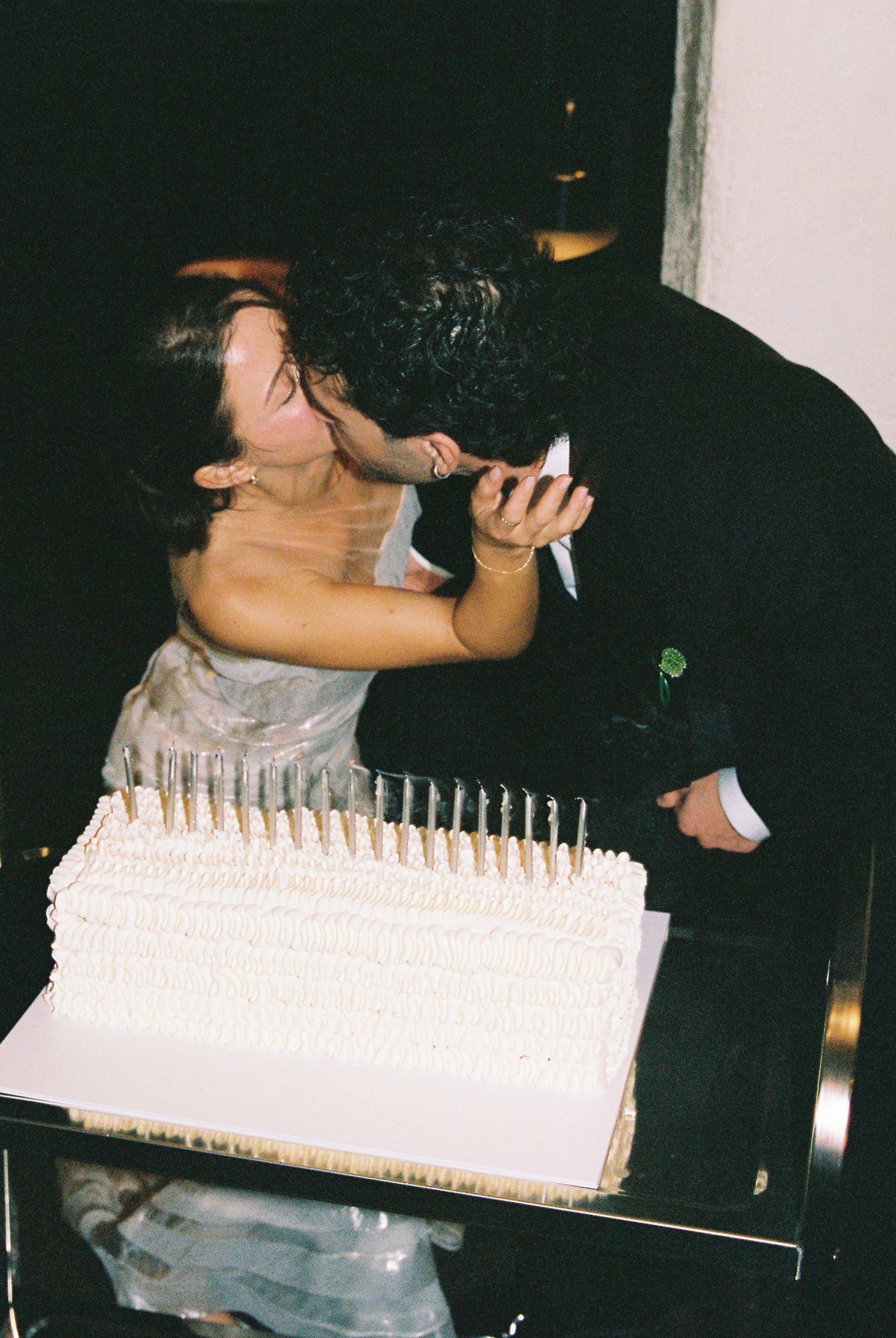Bride and groom sharing a kiss while cutting their white wedding cake with candles.