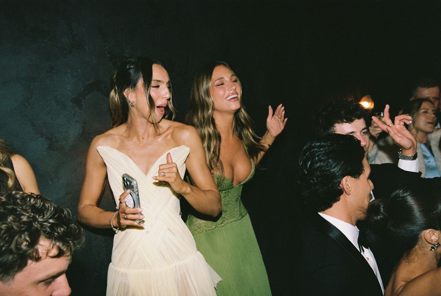 Bride in white dress and bridesmaid in green gown dancing joyfully at wedding reception party.