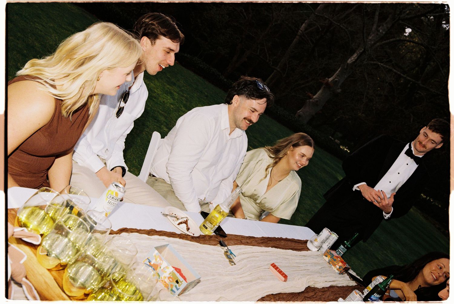 Guests gather around a white tablecloth table during an outdoor wedding reception at night.