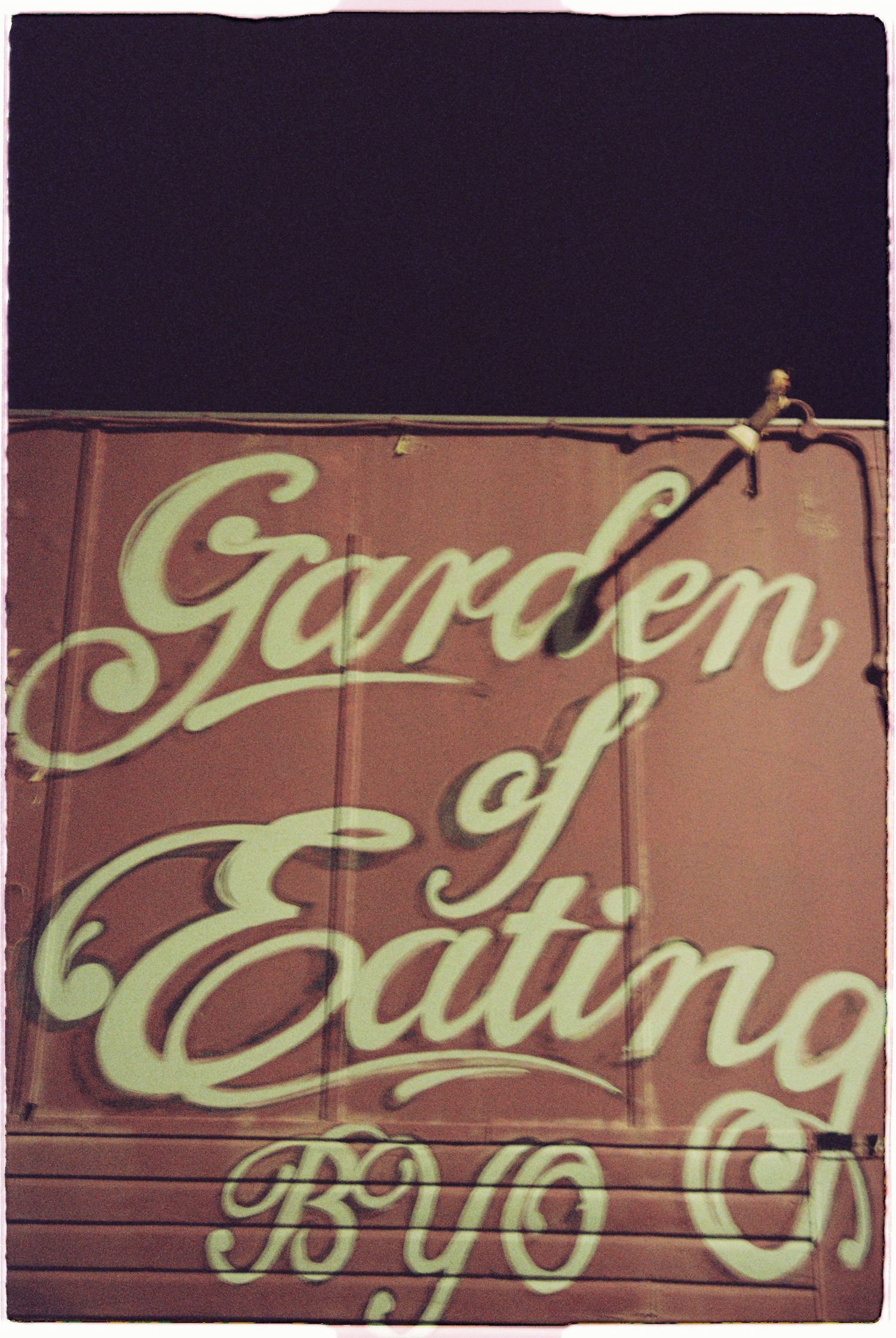 A vintage-style painted sign reading Garden of Eating BYO on a brown wall at a restaurant venue.