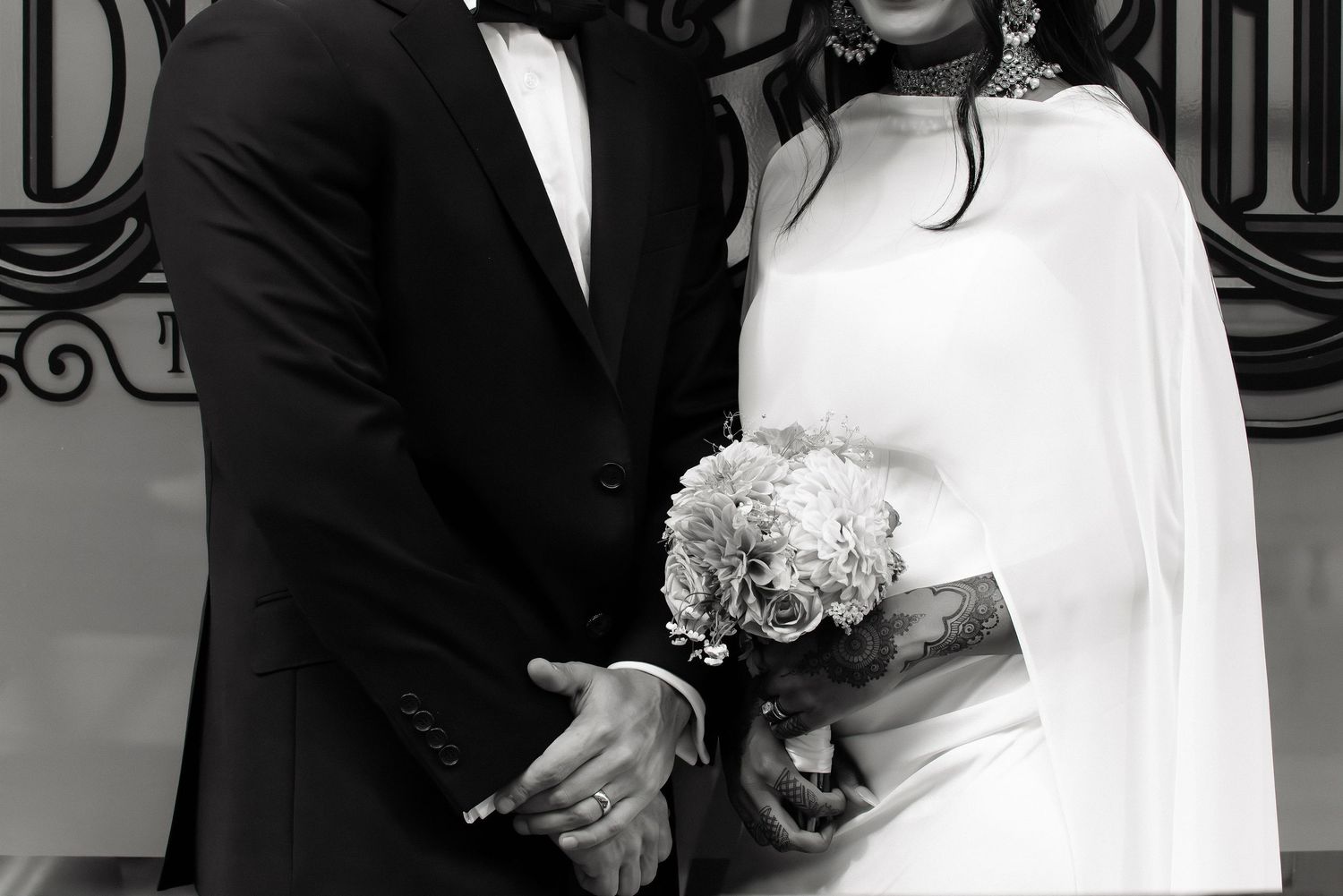 Black and white portrait of bride holding bouquet and groom embracing outside vintage venue.