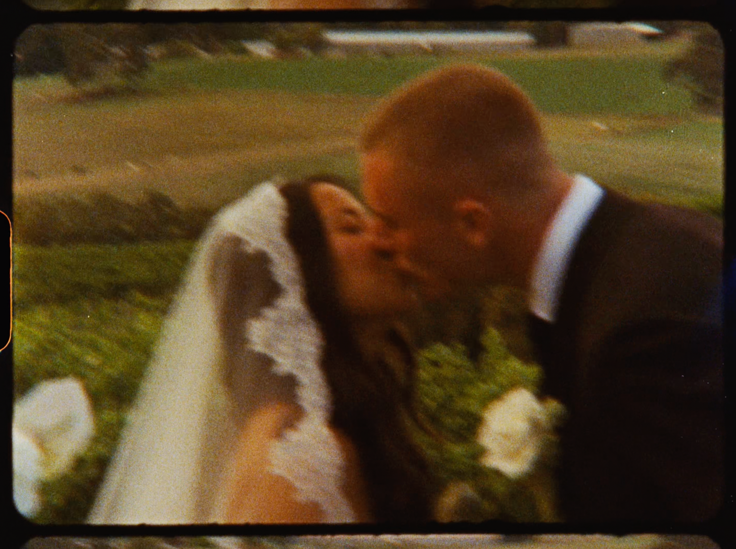Bride and groom sharing a romantic first kiss during outdoor wedding ceremony with green fields in background.