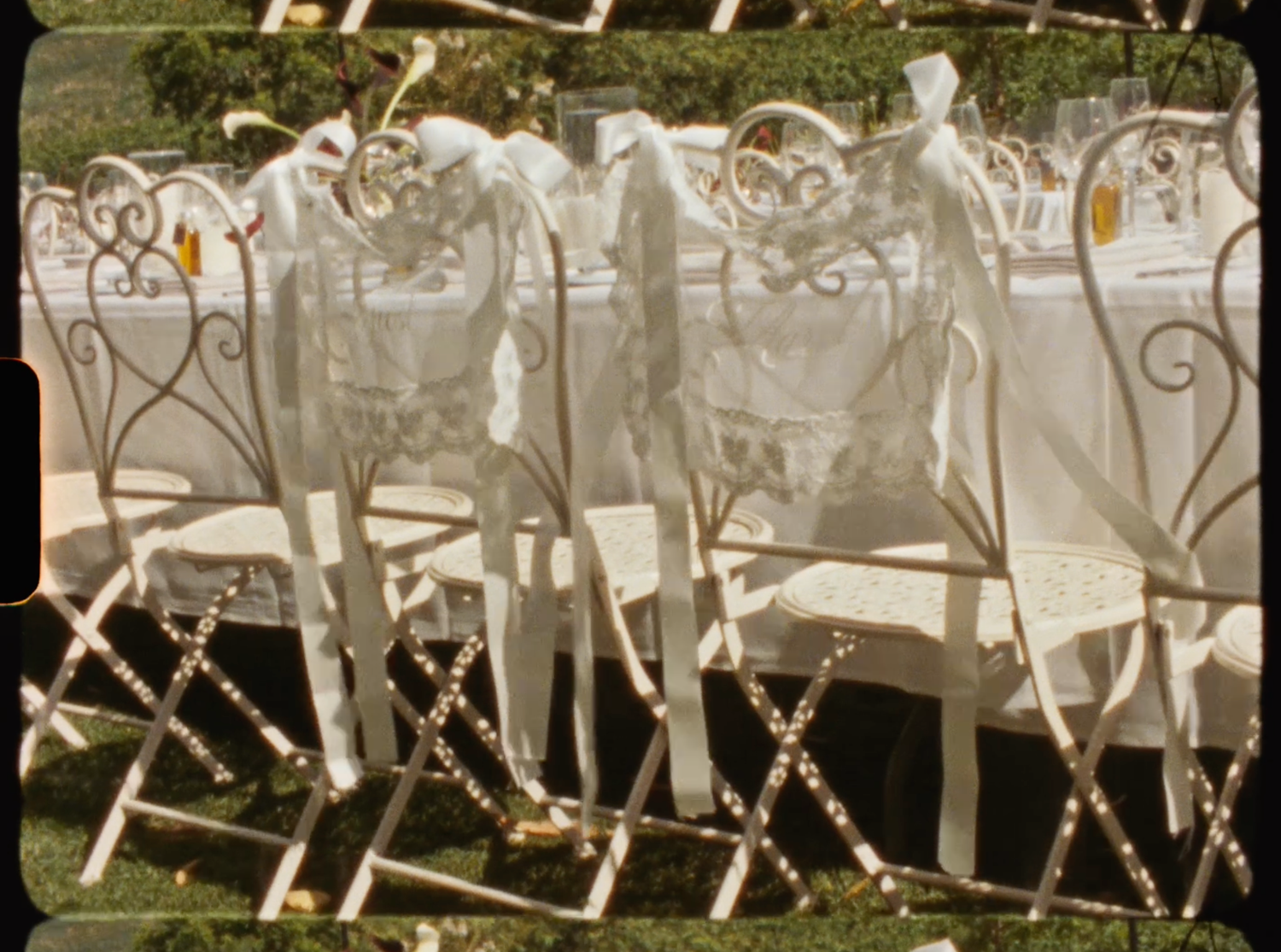 Ornate white wrought iron chairs with sheer fabric decorations arranged for an outdoor wedding ceremony.