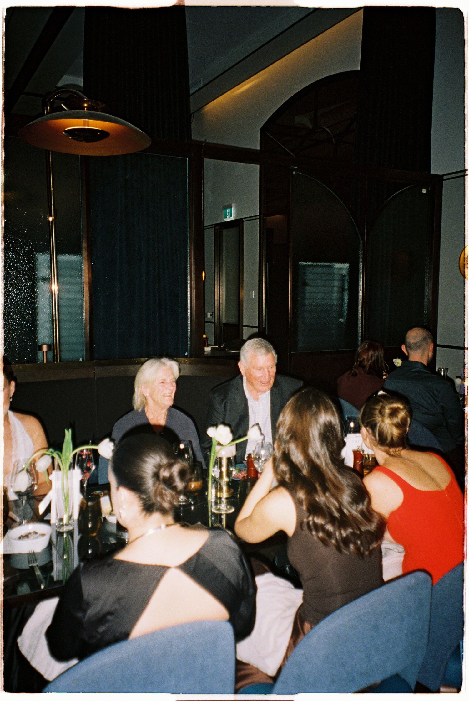 Wedding guests enjoy dinner conversation at a sophisticated dark-interior restaurant reception venue.