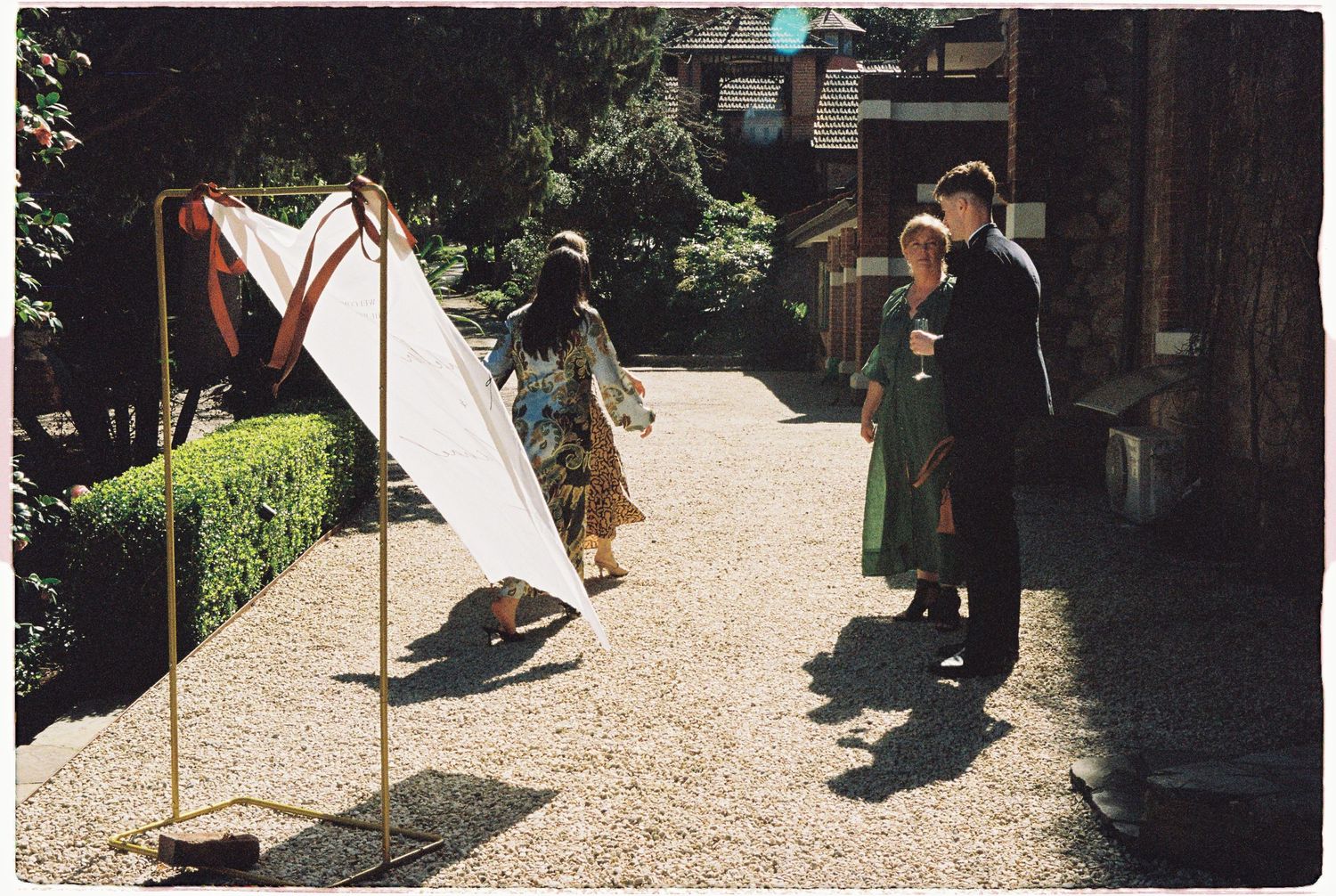 Guests admire an outdoor art installation with a white triangular frame at a garden wedding venue.