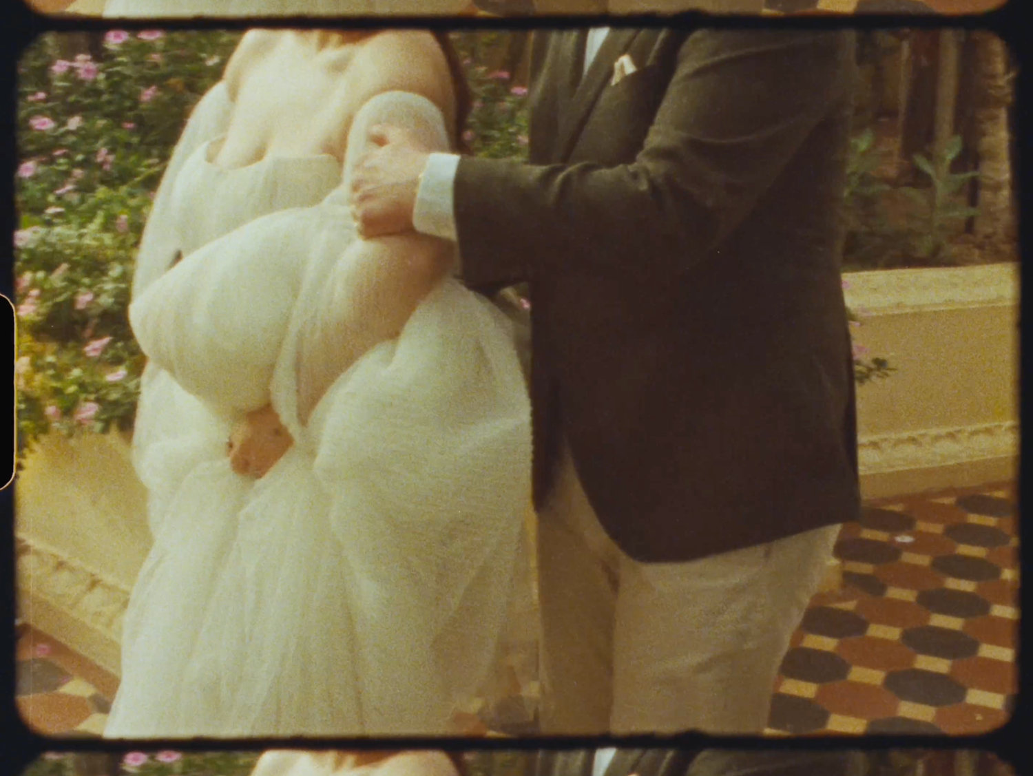 Close-up of bride in white gown holding hands with groom in dark blazer outdoors.