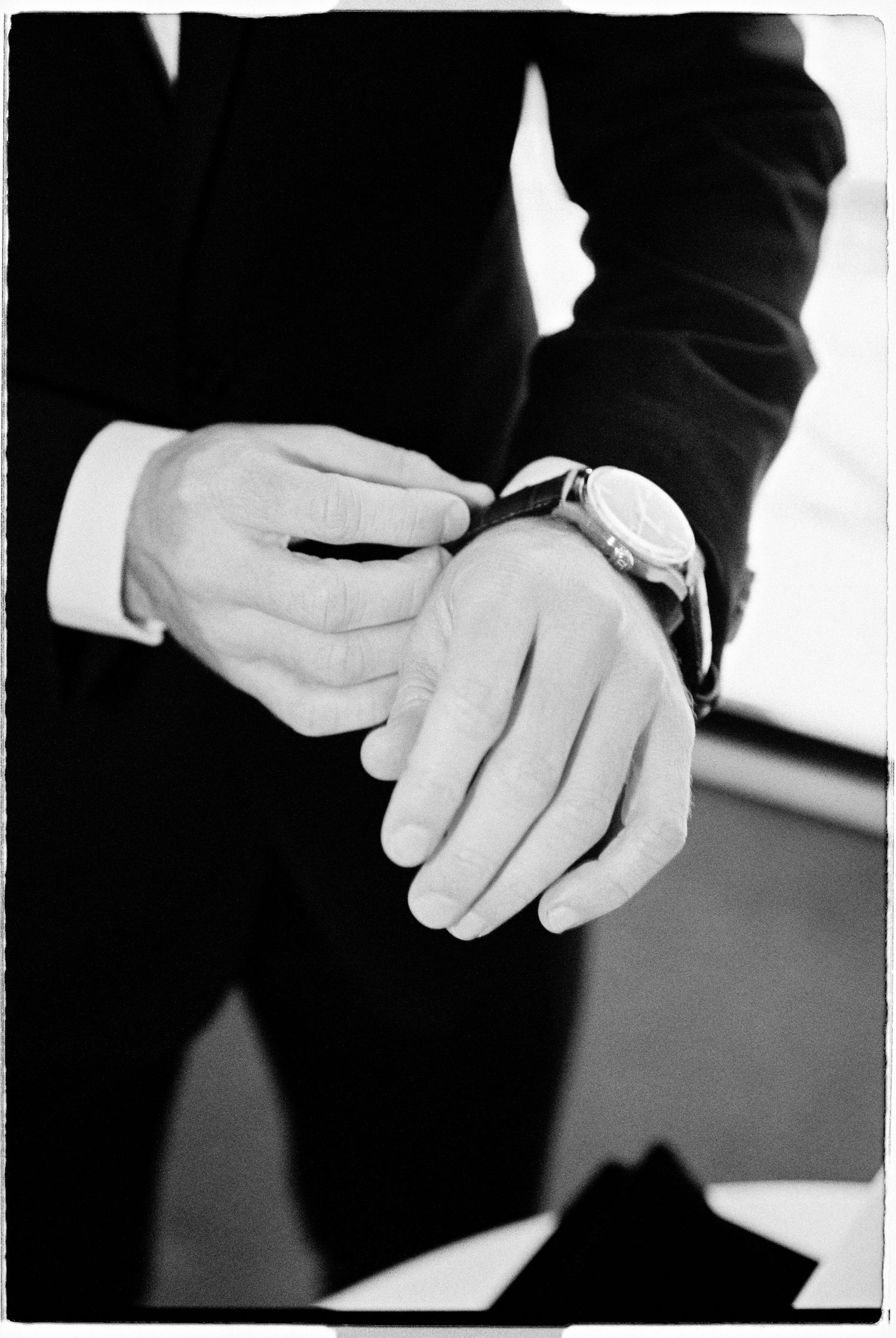A groom in a black suit adjusting his watch before the wedding ceremony.