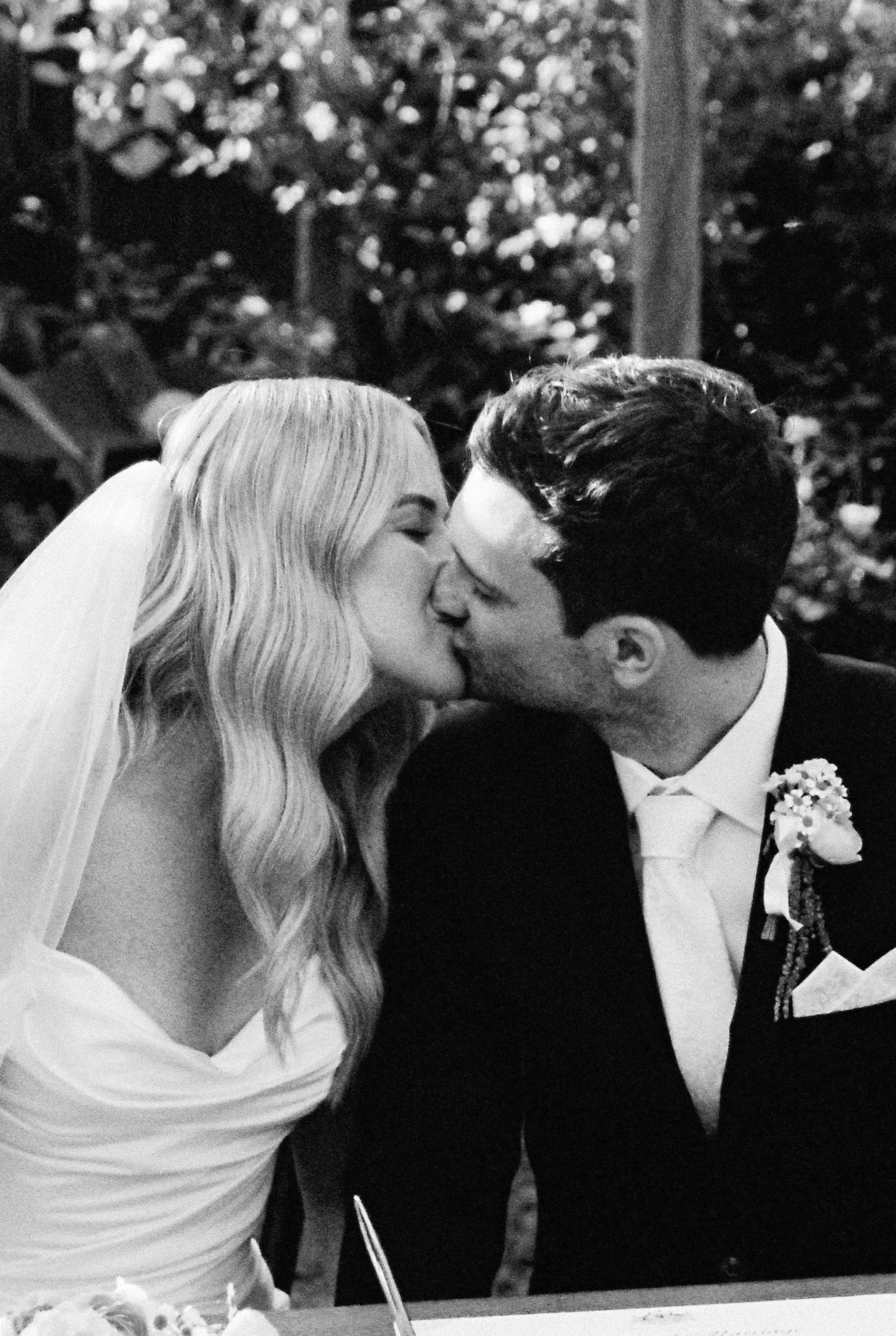Black and white photo of a bride and groom sharing a kiss at their outdoor wedding ceremony.