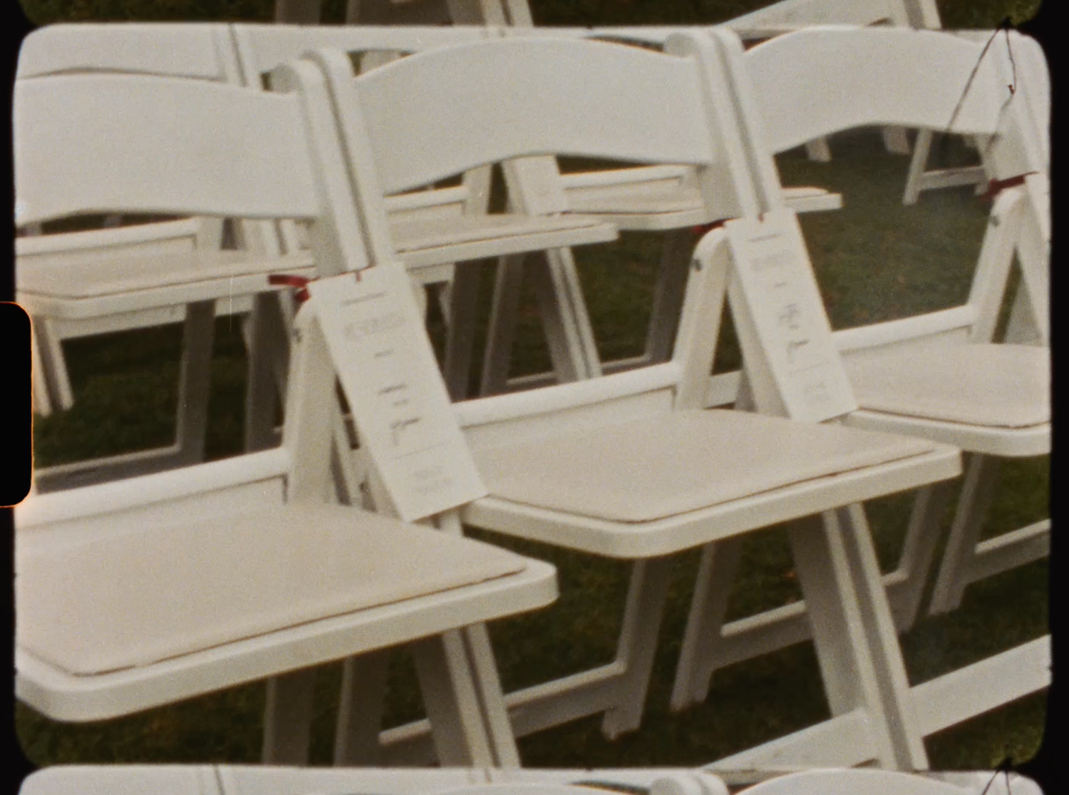 Rows of white folding chairs set up outdoors for a wedding ceremony on green lawn.