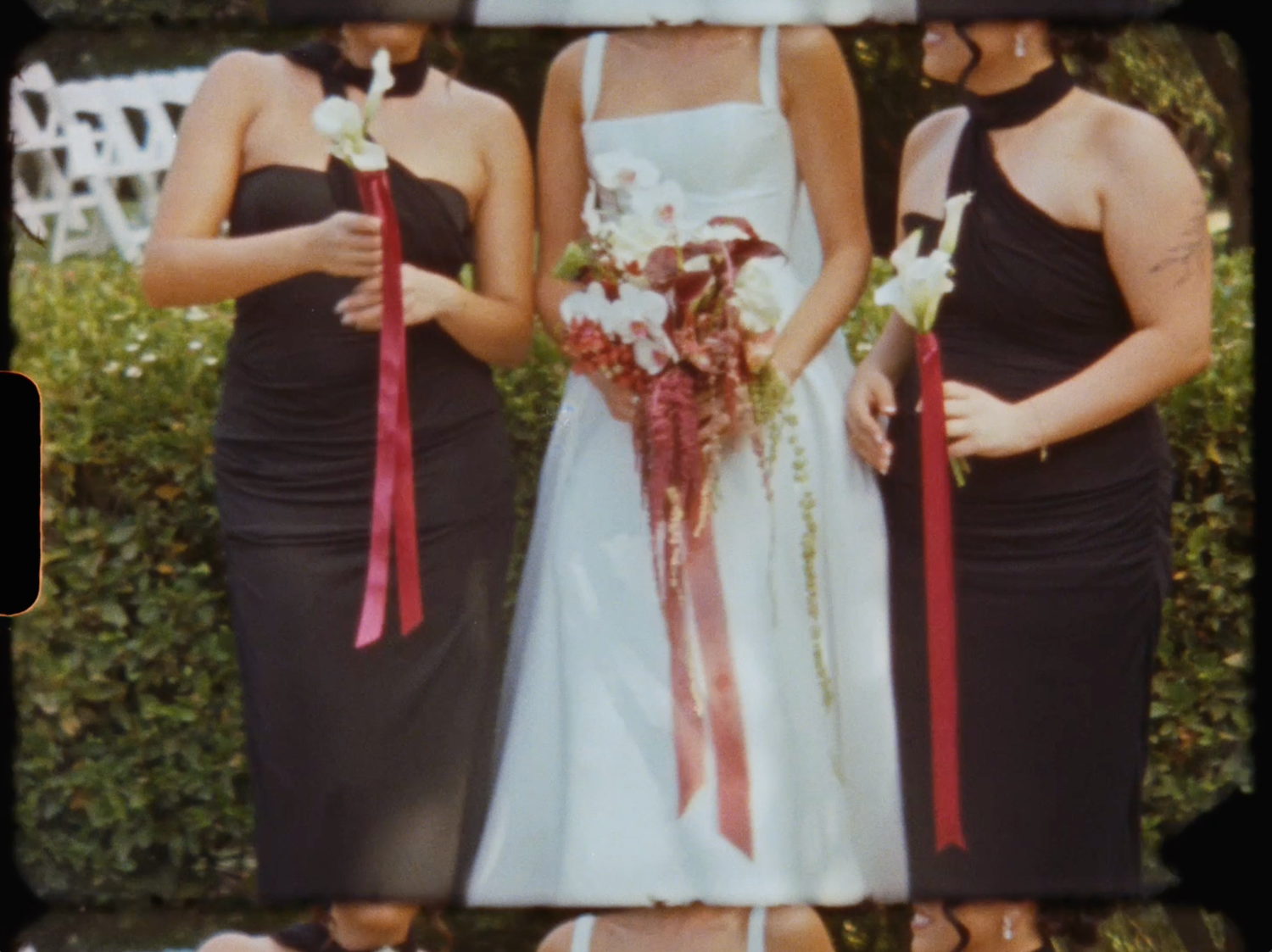 Bride in white dress with two bridesmaids in black halter dresses holding bouquets at outdoor wedding.