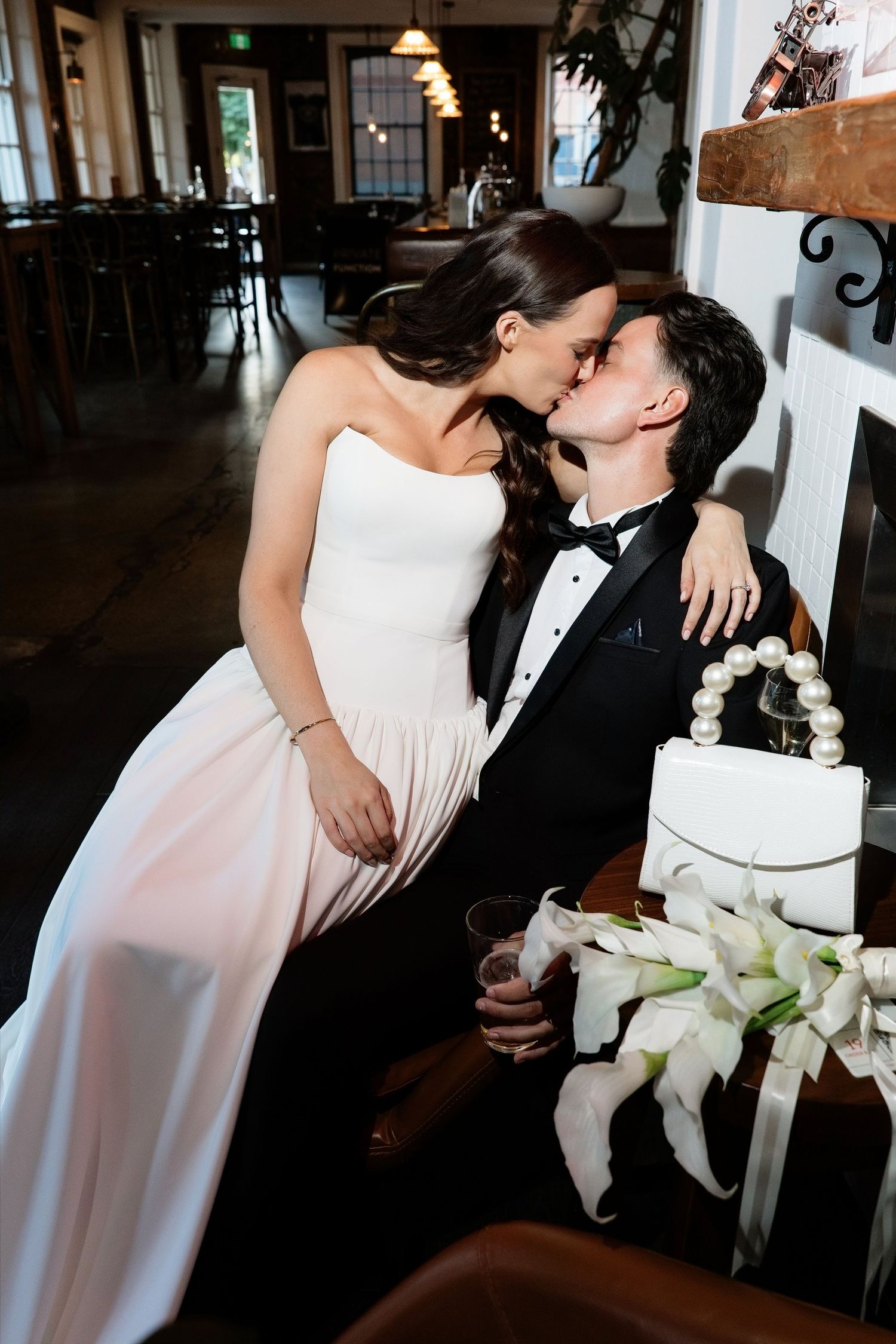 Bride and groom sharing a kiss while seated in a cozy indoor venue on their wedding day.