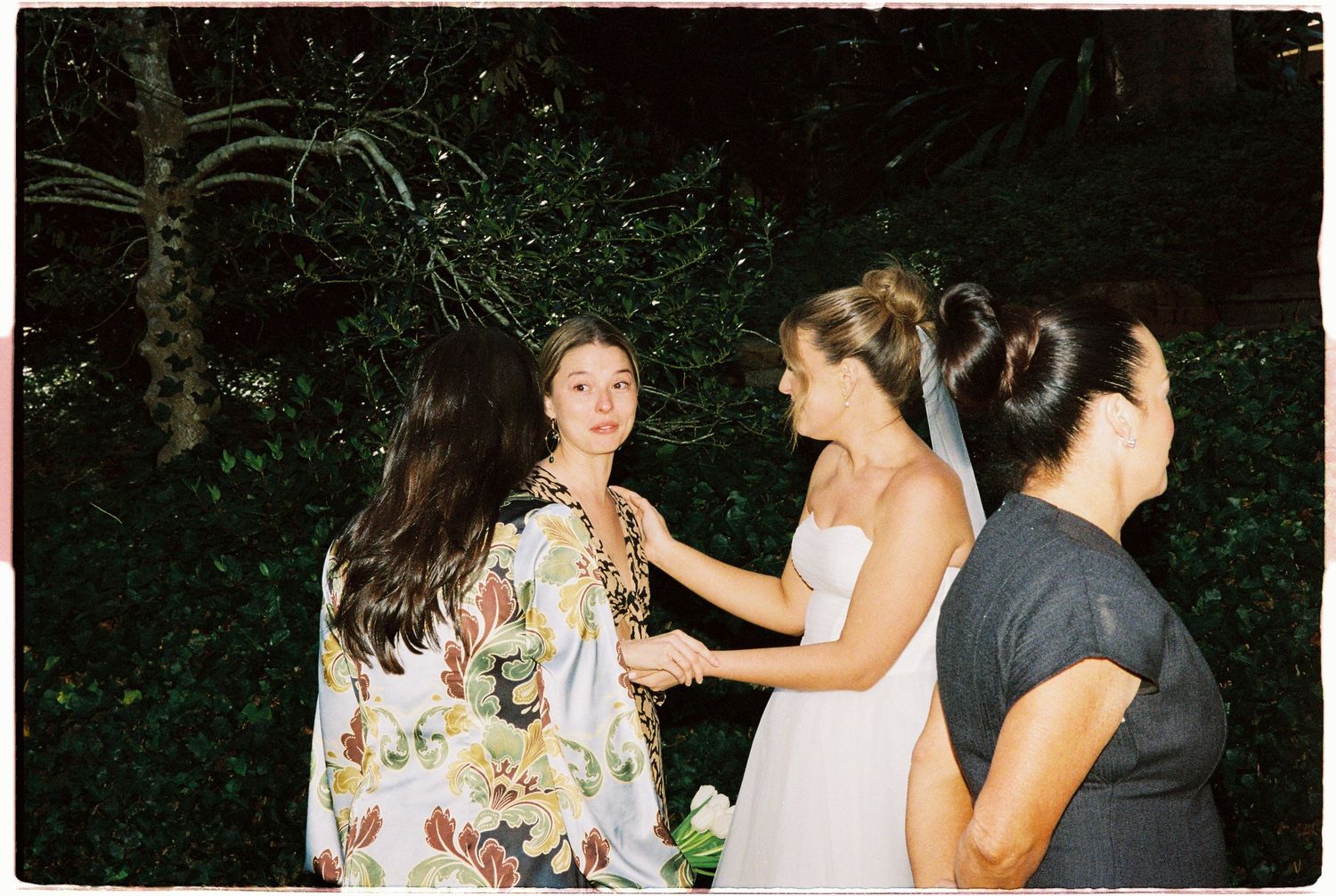 Bride in white dress chatting with guests in floral outfit at evening garden wedding.