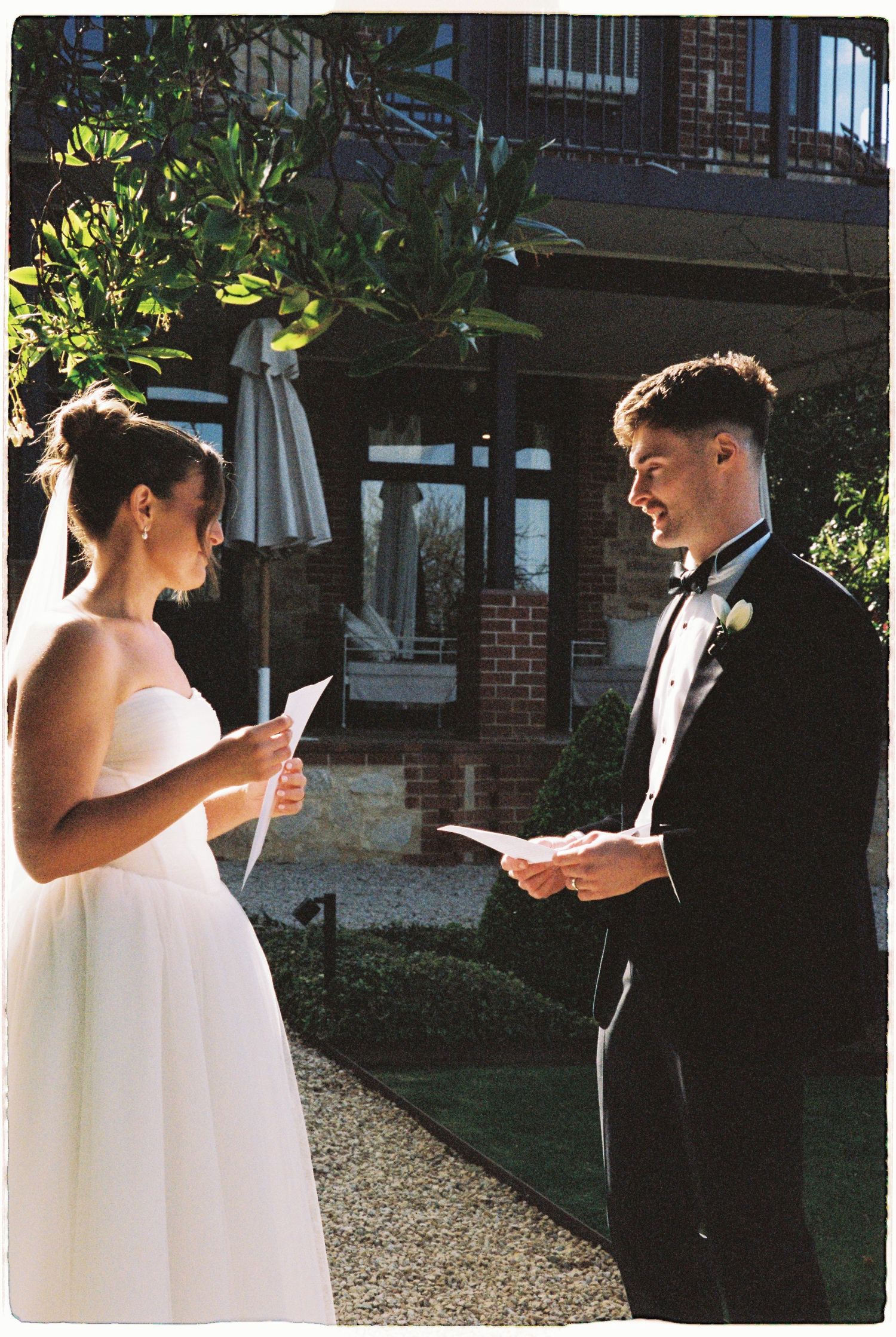Bride and groom exchange vows outdoors, reading from papers during intimate wedding ceremony.