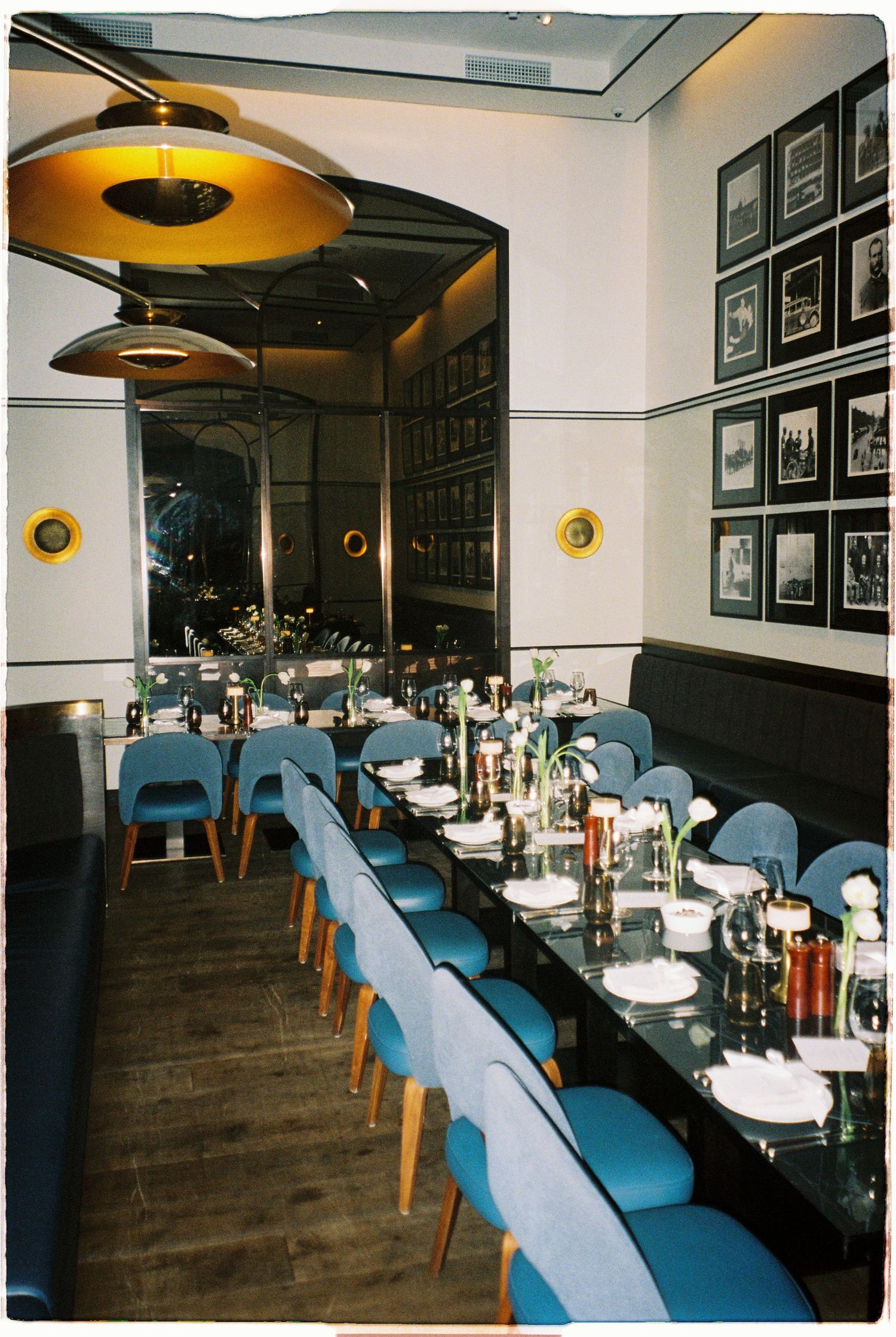 Elegant restaurant dining room with blue velvet chairs, black tables, and gold pendant lights.