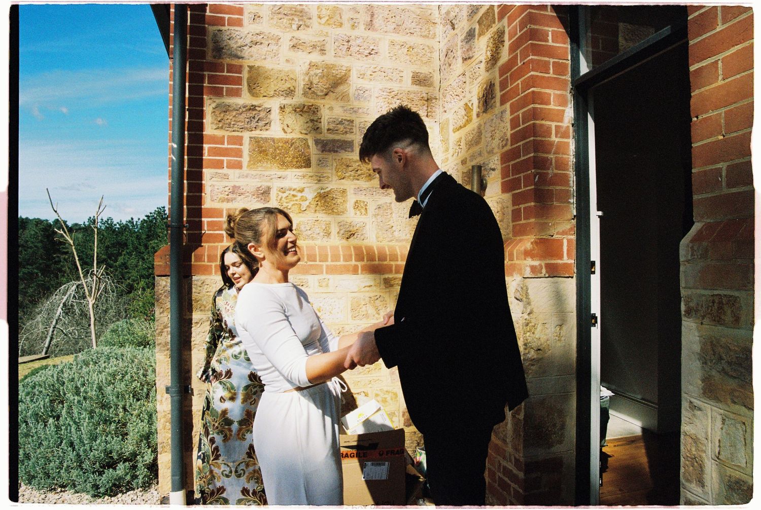 Bride and groom exchanging vows outside a rustic stone and brick chapel surrounded by lush greenery.