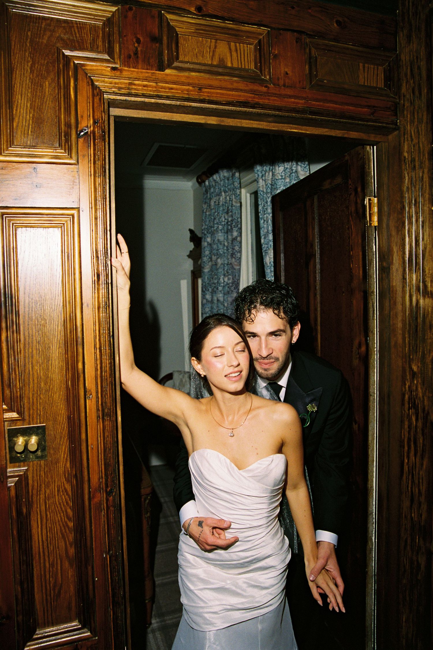 Bride and groom sharing a joyful moment in an ornate wooden doorway on their wedding day.