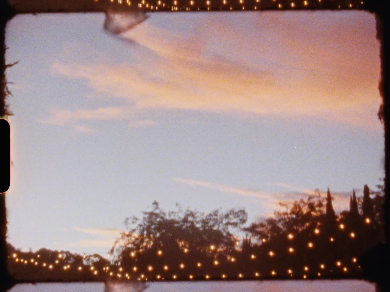 Soft pink sunset sky with string lights glowing above silhouetted trees.